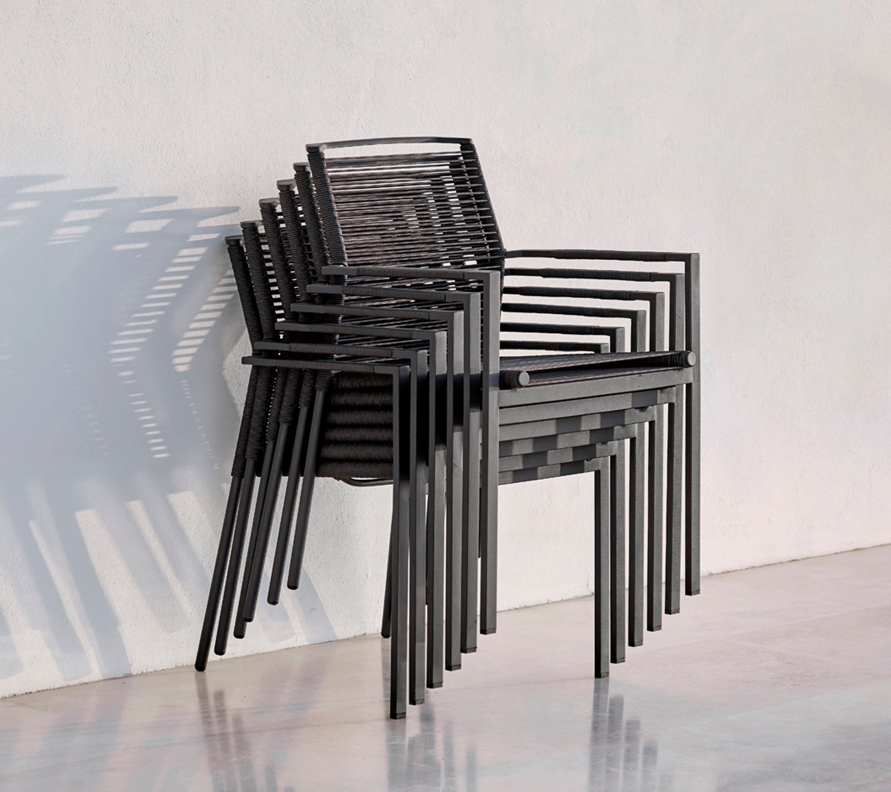 Een stapel moderne zwarte stoelen met een strak ontwerp, die schaduwen werpen tegen een lichte achtergrond.