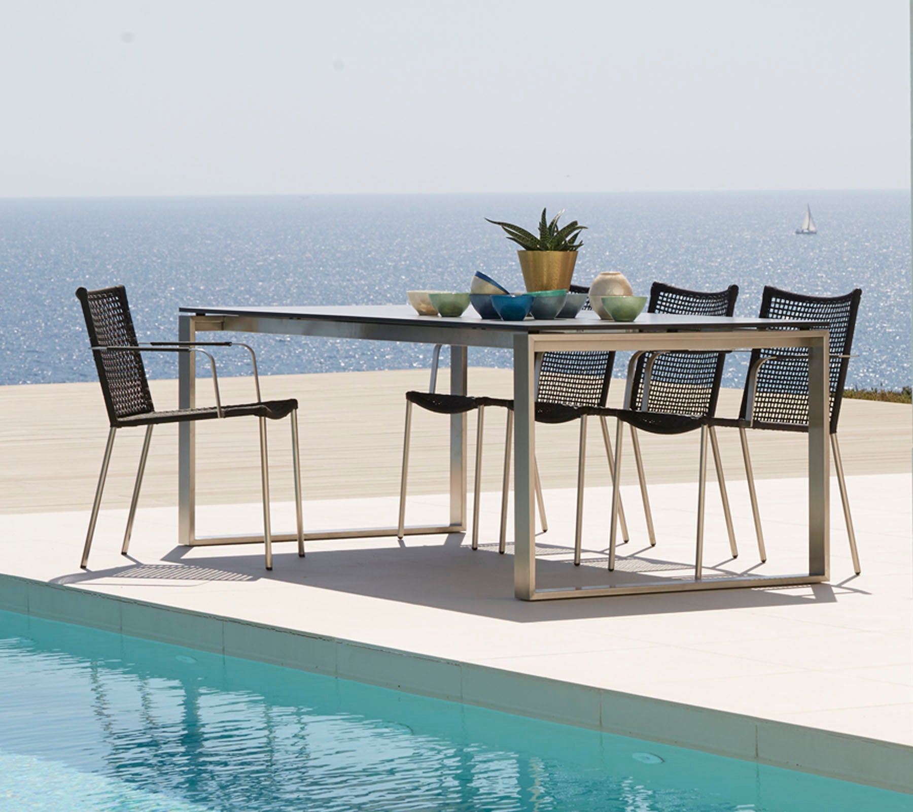 Een moderne eettafel omringd door stijlvolle stoelen, versierd met decoratieve artikelen, met uitzicht op een rustige zee.
