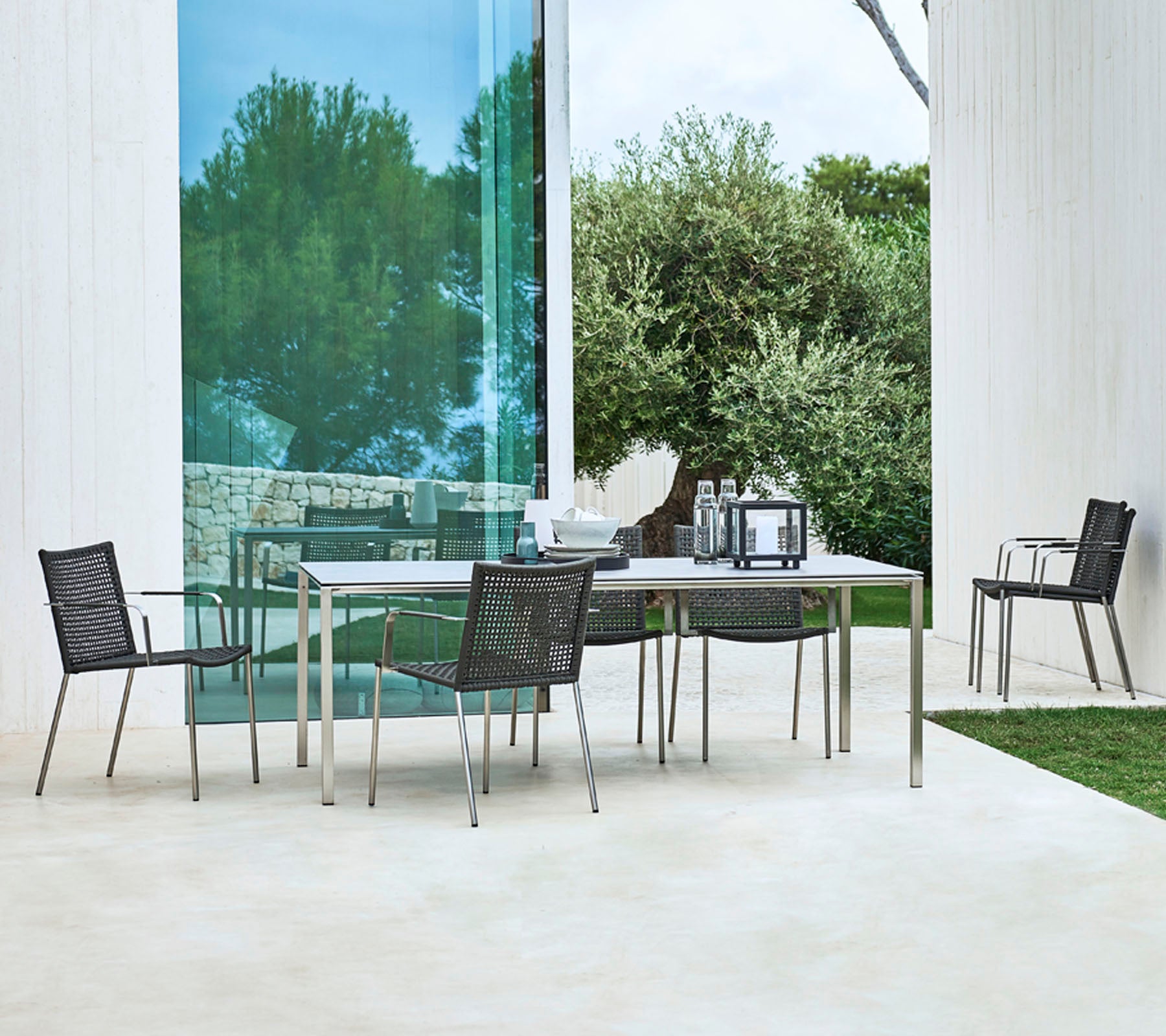Een modern buitentafelsysteem met een rechthoekige tafel en vier stijlvolle stoelen met een strak ontwerp, omringd door groen.
