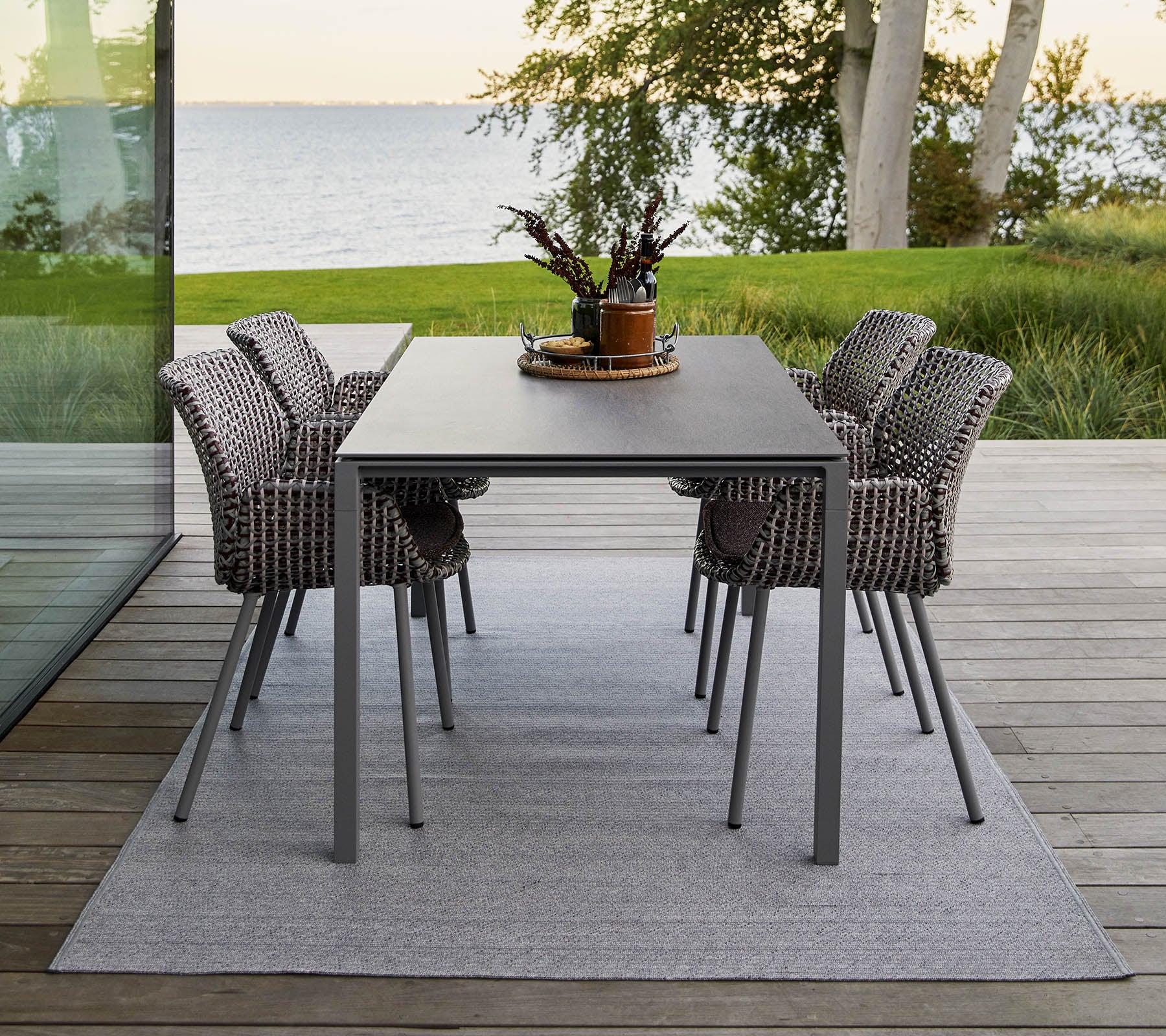 Een moderne eettafel met vier stijlvolle, geweven stoelen, versierd met een decoratief plantenmiddelpunt op een zacht tapijt.