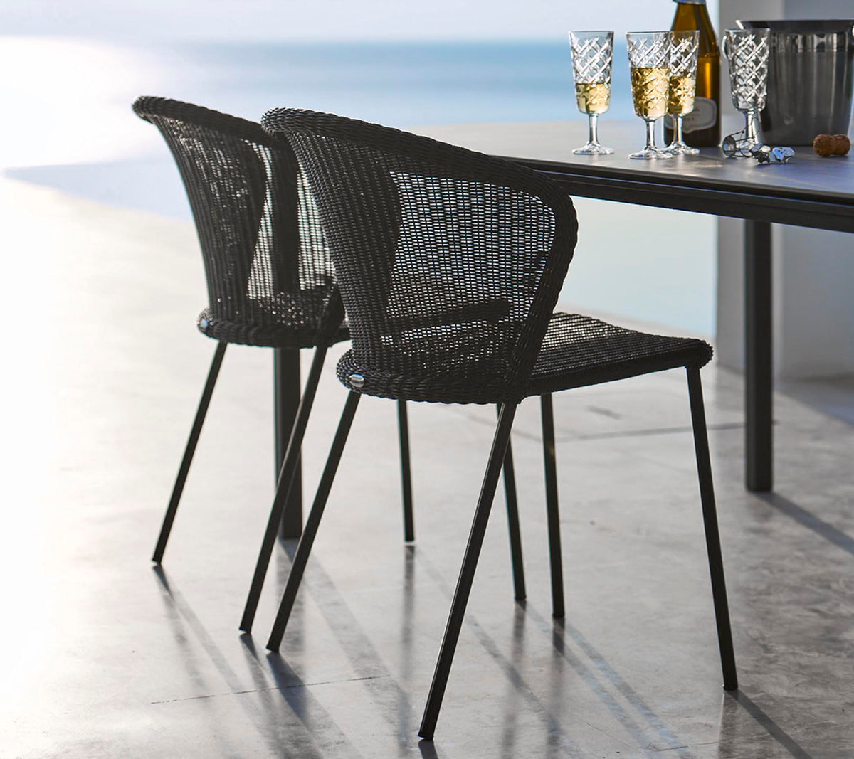 Twee stijlvolle zwarte gevlochten stoelen naast een tafel gedekt met glazen en een fles, die een ontspannen eet sfeer oproept.