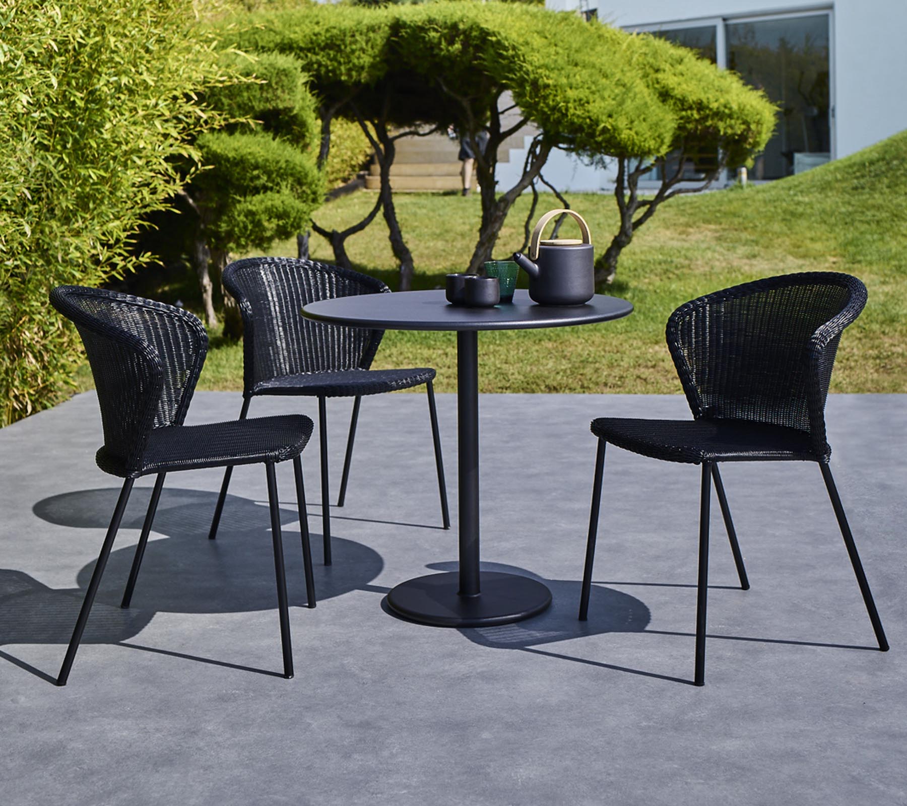 Een moderne tuinset met een ronde tafel en drie zwarte gevlochten stoelen, compleet met een theepot en kopjes op de tafel.