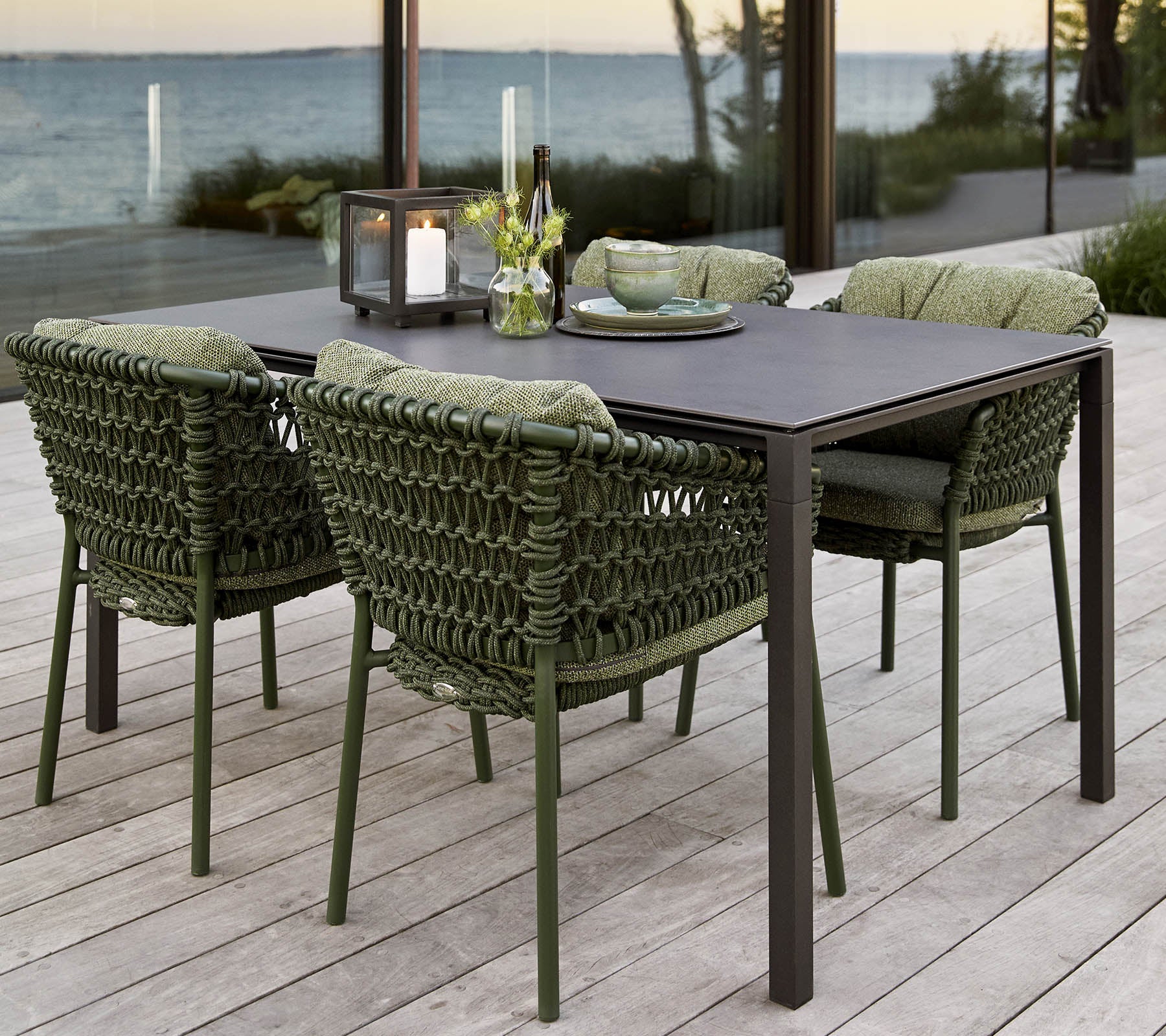 Stijlvolle buiten eetset met een rechthoekige tafel en vier gewatteerde, gevlochten stoelen, aangevuld met een bloemstuk als middelpunt.
