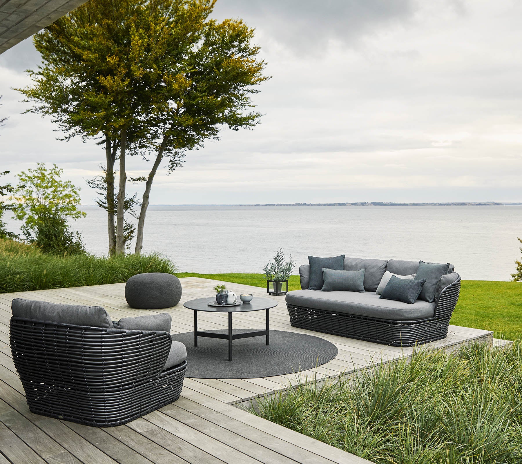 Gezellige zitgelegenheid met een bank en stoelen rond een ronde tafel, omringd door groen en uitzicht op het water.
