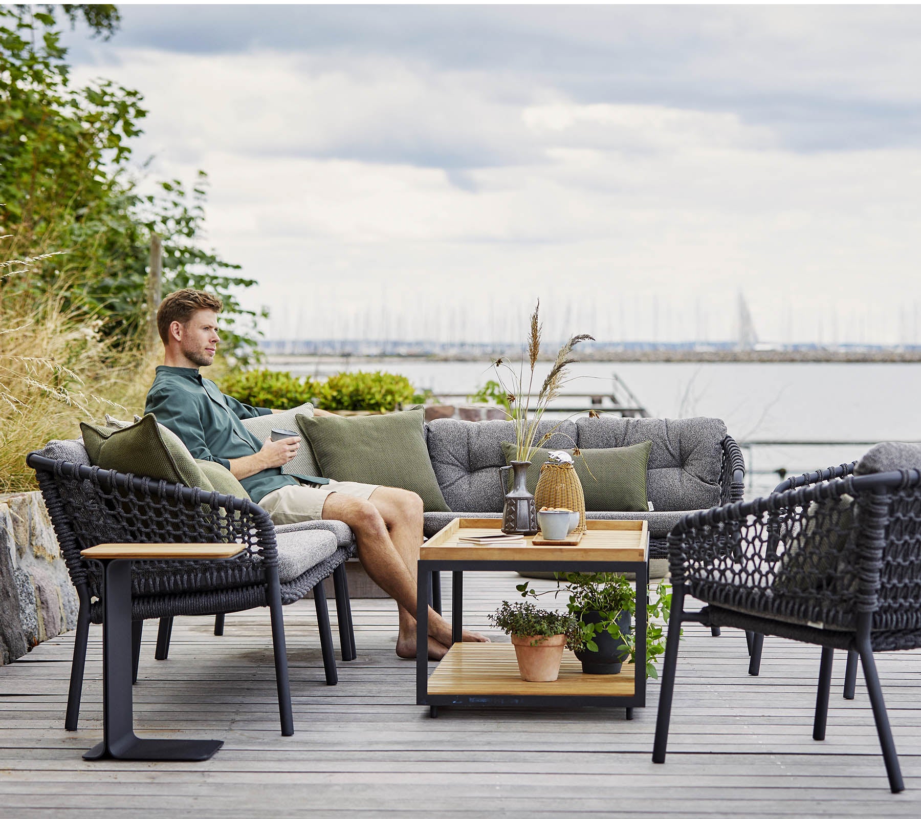 Een comfortabele zitruimte met een man die ontspant, met stijlvolle rieten stoelen en een houten salontafel versierd met planten en decoratieve items.