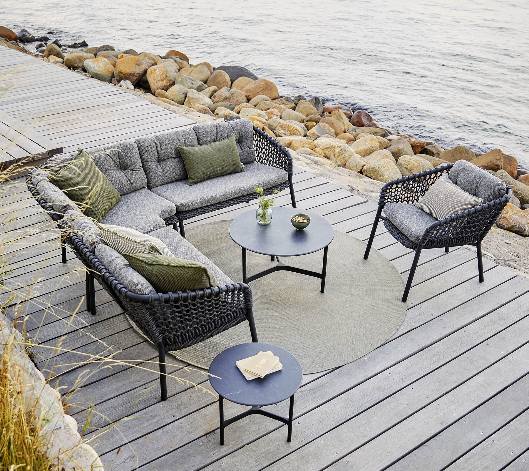 Een stijlvolle buitenzitgroep met een modulaire bank en stoelen met grijze kussens, een ronde tafel en decoratieve accenten.