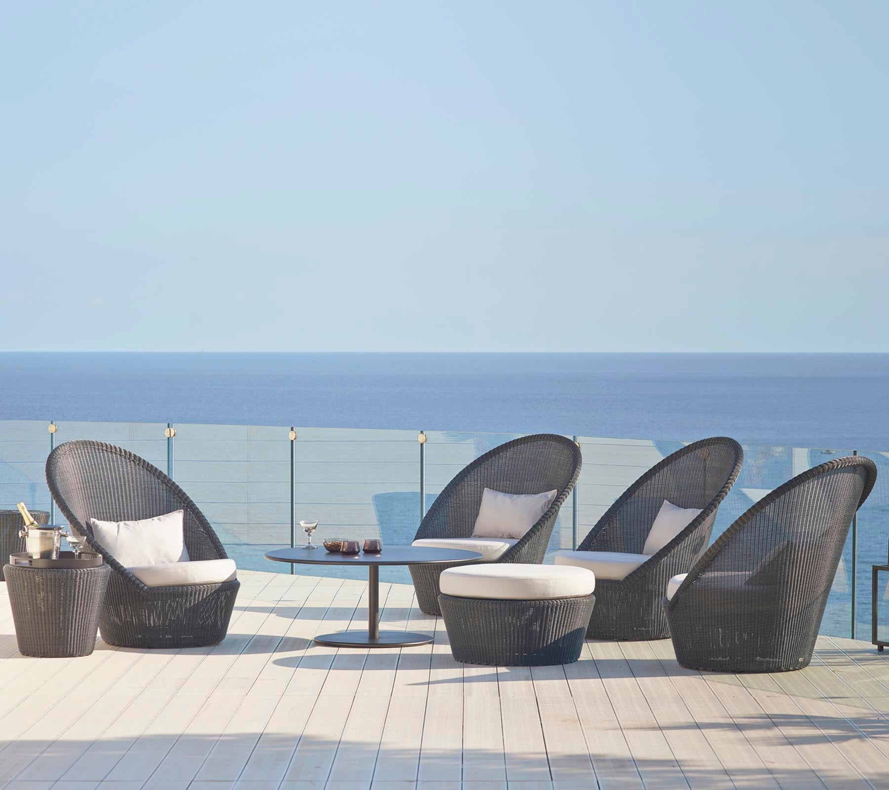 Stijlvolle zitset met gebogen stoelen en een bijpassende tafel, tegen een serene oceaanachtergrond. Ideaal voor ontspanning.