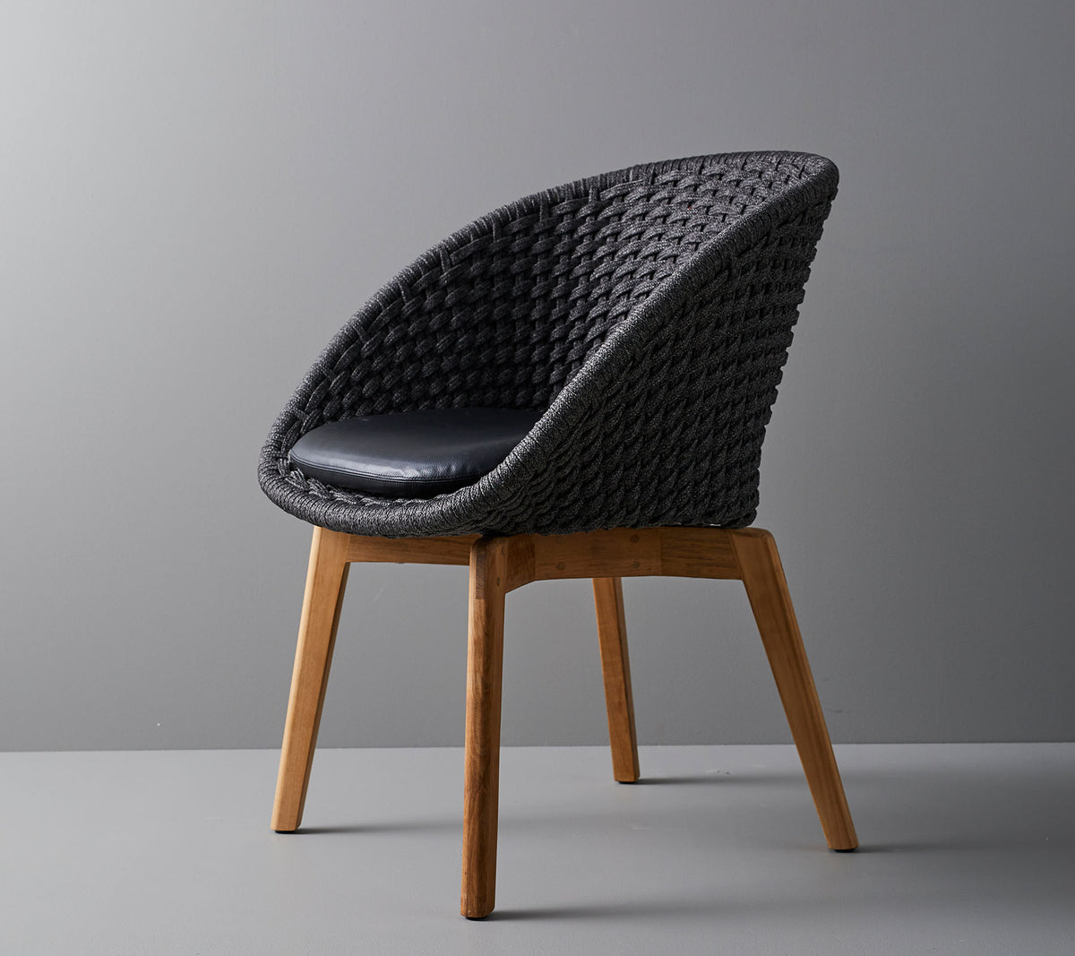 Stijlvolle geweven stoel met een comfortabel kussen, met coole, taps toelopende houten poten en een modern ontwerp dat geschikt is voor verschillende omgevingen.