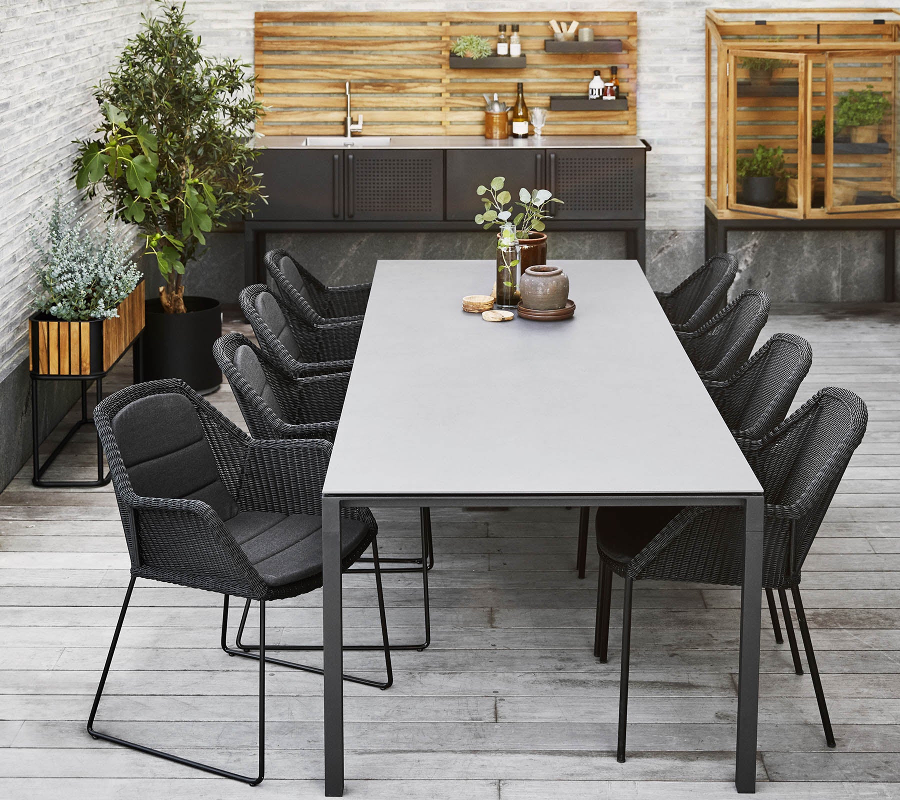Een moderne eetopstelling met een lange tafel omringd door slanke zwarte stoelen, aangevuld met decoratieve planten en een houten achtergrond.