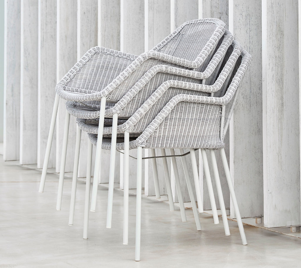 Gestapelde moderne stoelen met een geweven ontwerp in grijs en wit, leunend tegen verticale oppervlakken, en een strakke en minimalistische esthetiek tentoonstellend.