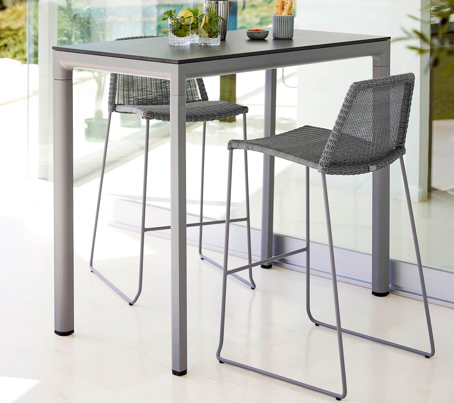 Een strak tafeltje met twee hoge krukken, met een modern design en een lichte kleurstelling, aangevuld met een klein plantencentertje.