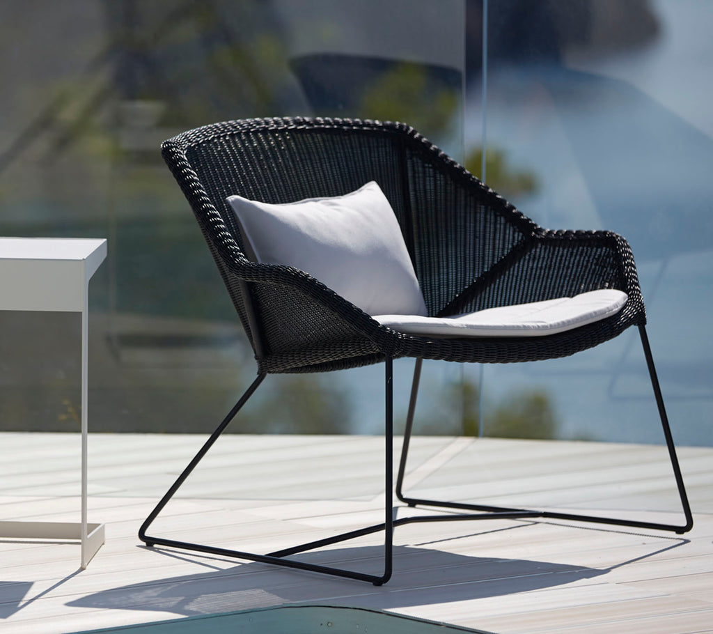 Moderne zwarte stoel met witte kussen in een stijlvolle buitenlounge-instelling.