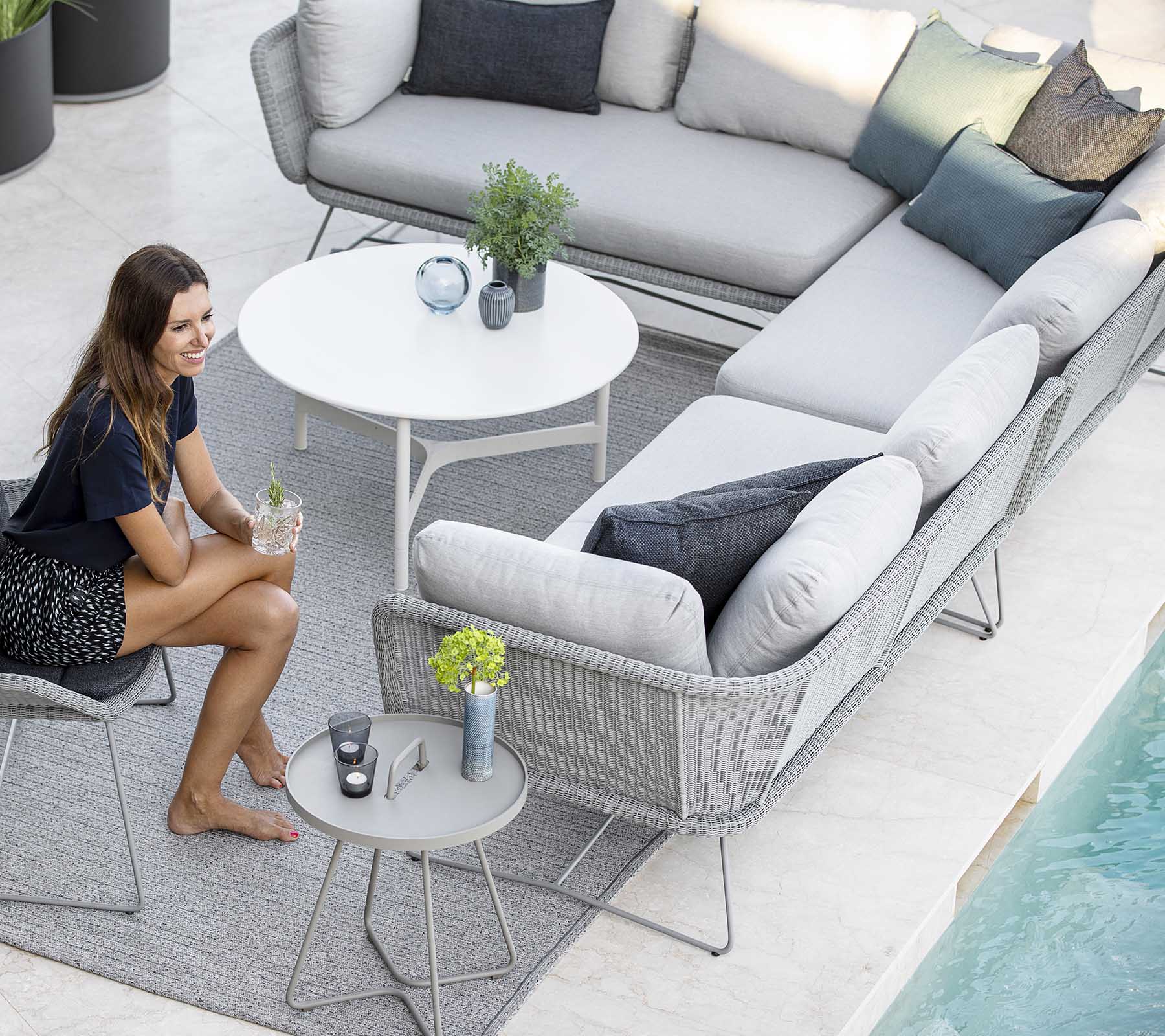 Een stijlvolle buitenzitarrangement met een sofa, accentkussens en een kleine tafel, aangevuld met planten en een zwembad in de buurt.