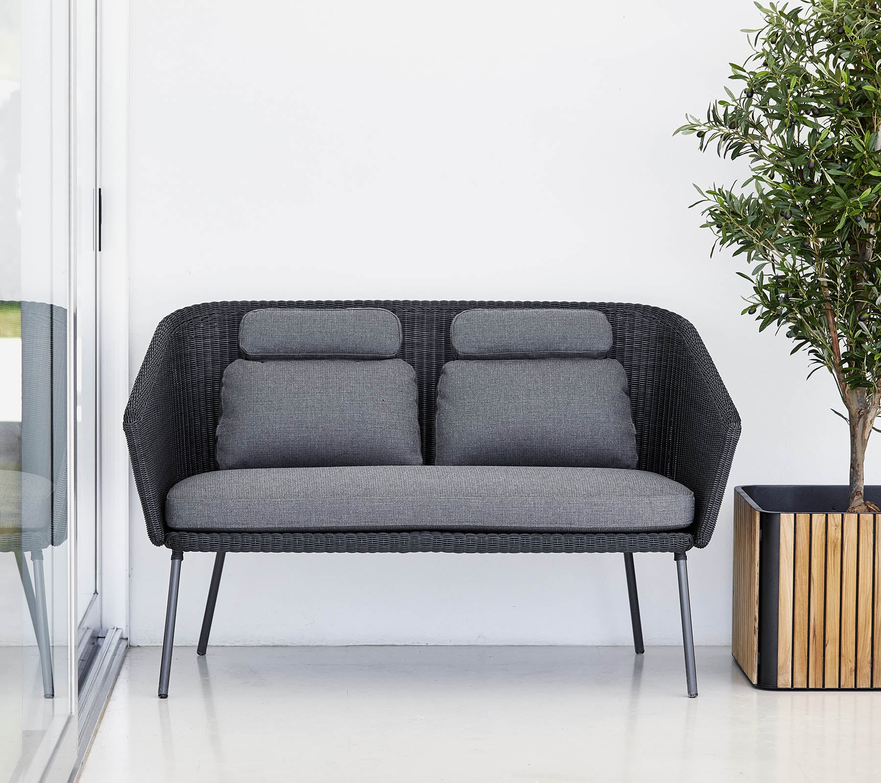Stijlvolle zwarte bank met grijze kussens, aangevuld met een kamerplant in een houten plantenbak. Modern en minimalistisch ontwerp.