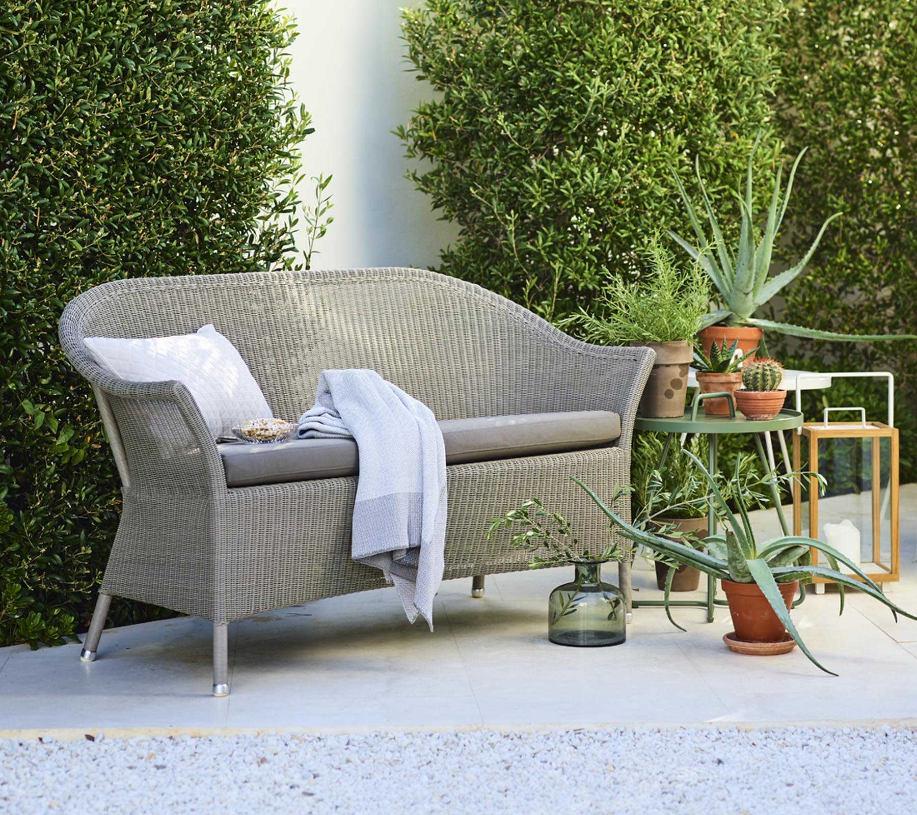Een gezellige loveseat met decoratieve kussens, vergezeld van potplanten en een side table, omringd door groen.