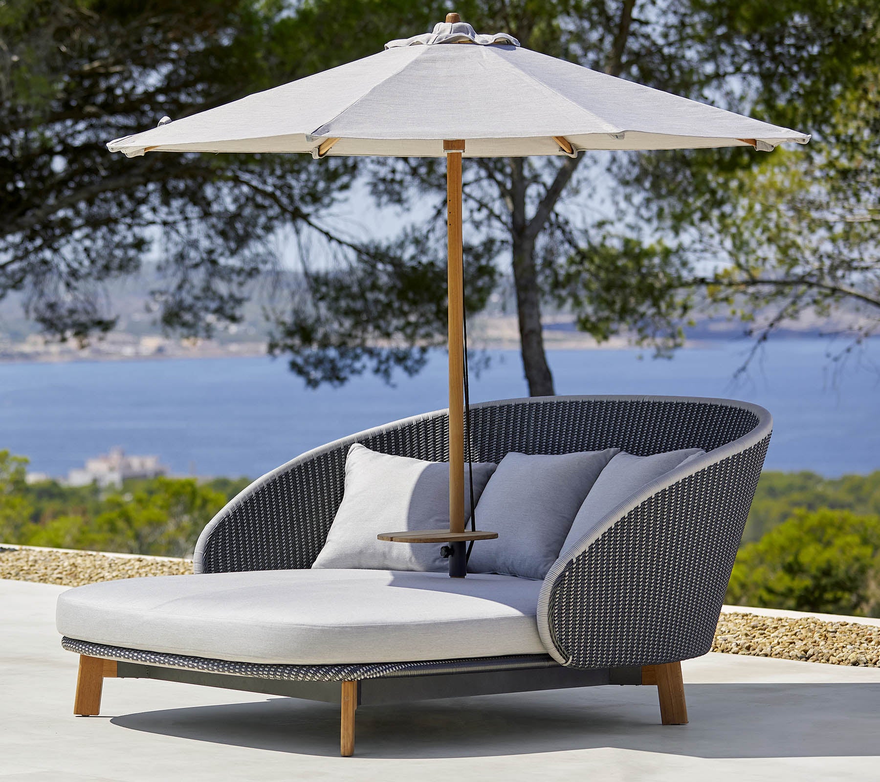 Stijlvolle loungestoel voor buiten met comfortabele kussens en een grote parasol voor schaduw, tegen een schilderachtige achtergrond.