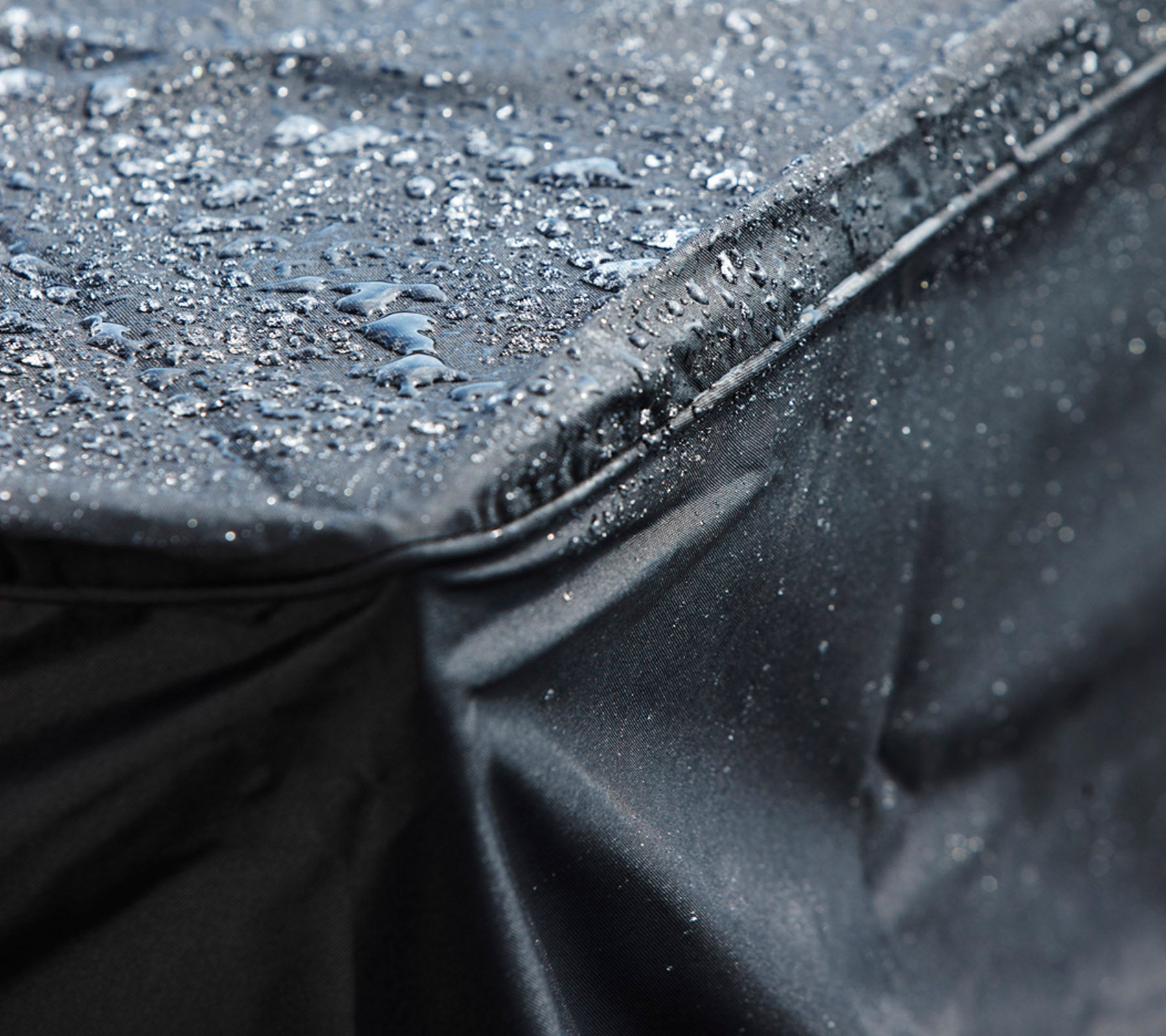 Close-up van een zwart waterdicht hoesje met waterdruppels op het oppervlak, waarmee het beschermende ontwerp wordt getoond.