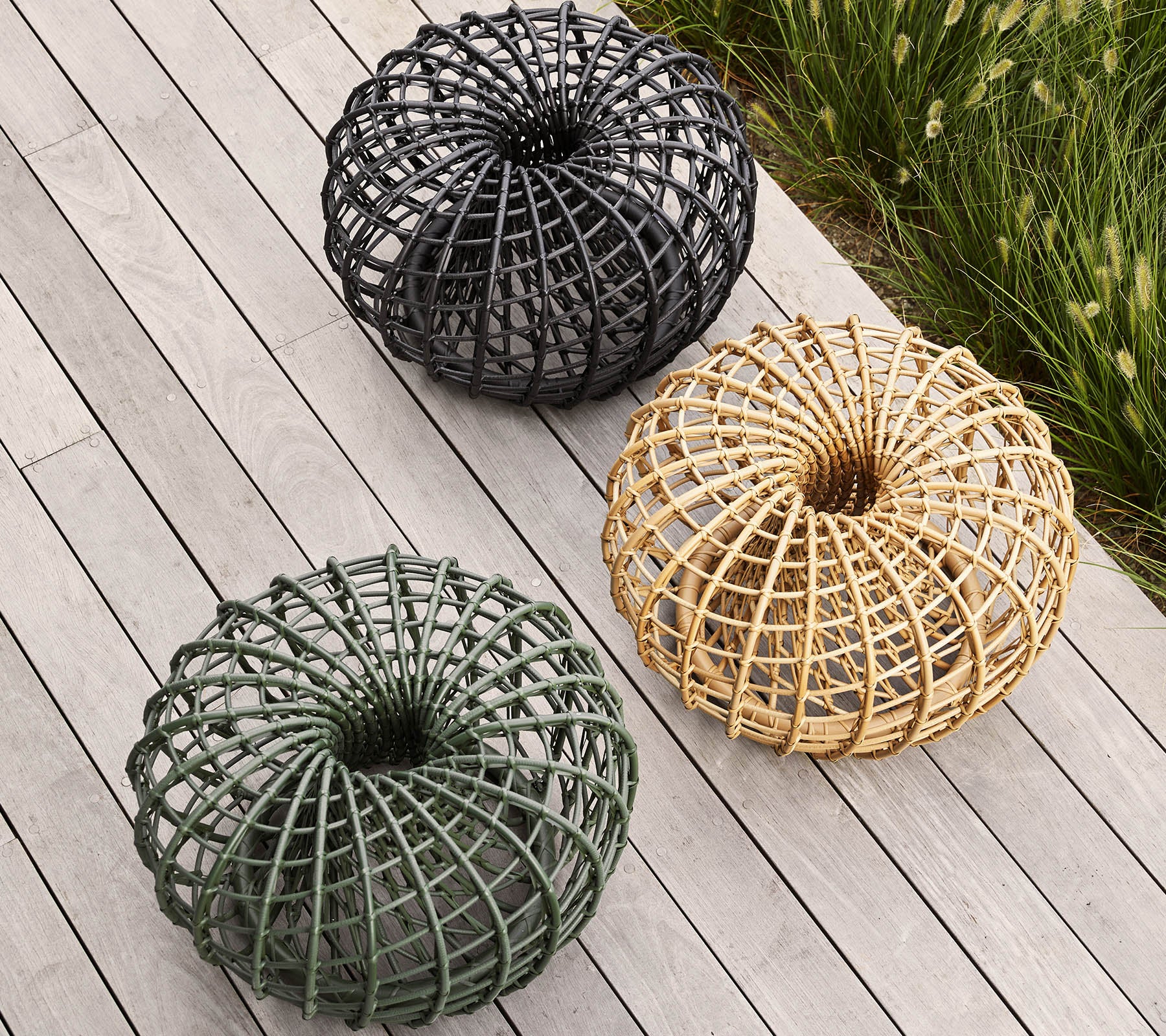 Drie gevlochten decoratieve manden in zwart, groen en natuurlijke tinten, gerangschikt in een cirkelvorm patroon op een houten oppervlak.