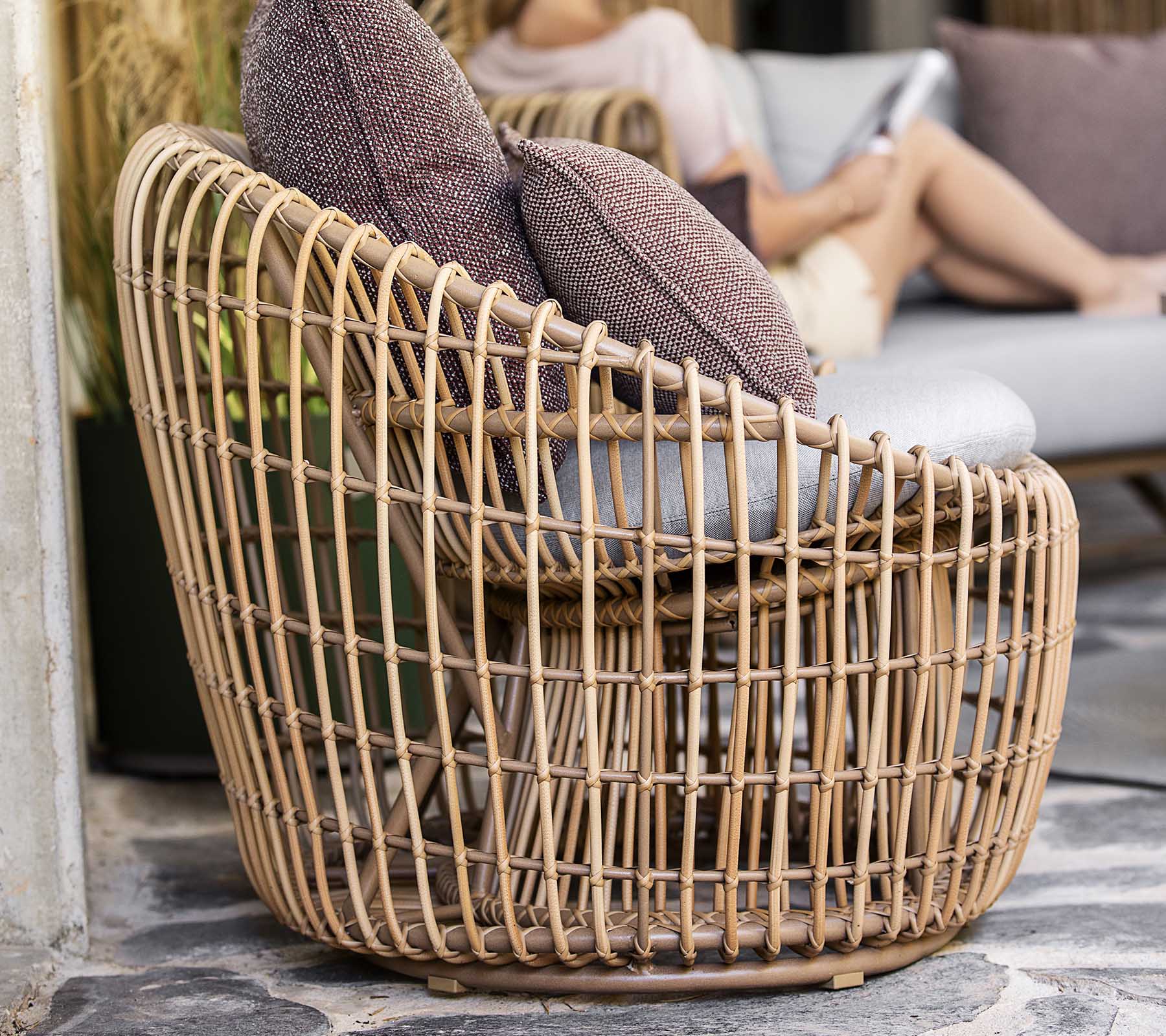 Een stijlvol, geweven stoel met een open ontwerp, voorzien van twee zachte kussens voor extra comfort. Perfect voor ontspannen zitten.