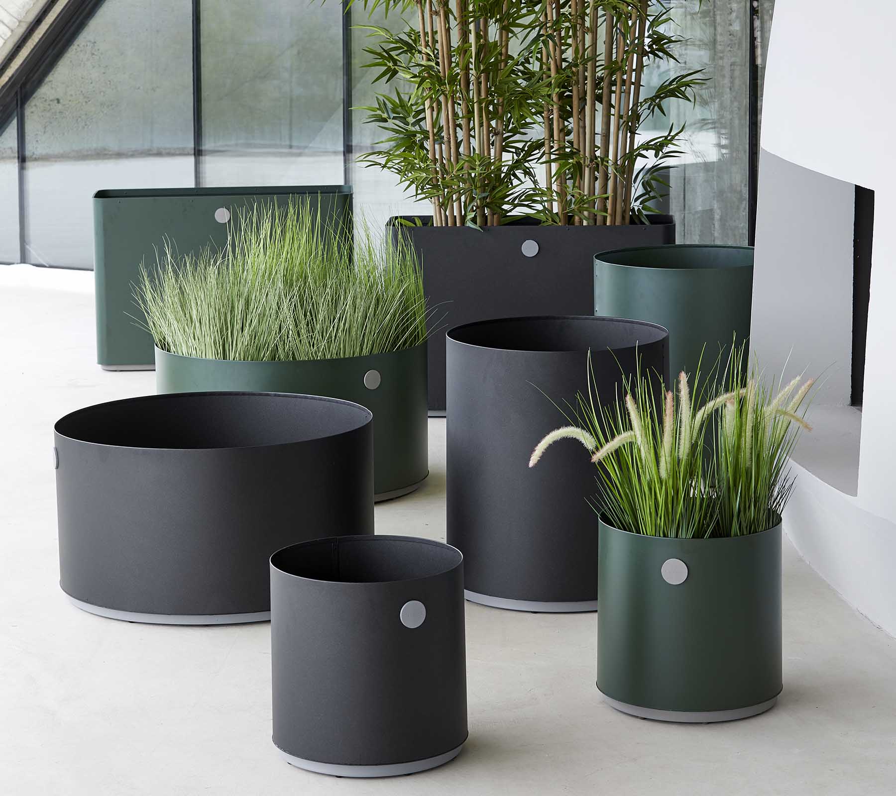 Diverse moderne plantenbakken in donkere tinten, met siergrassen en planten, gestyled in een elegante setting.