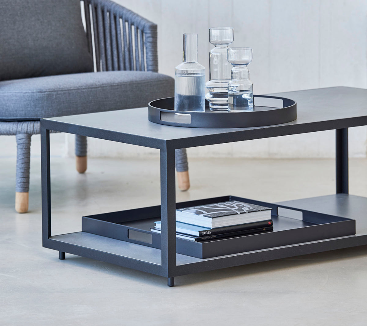 Modern salontafel met een strak design, met een dienblad, glazen en boeken op de onderste plank. Ideaal voor stijlvolle woonruimtes.