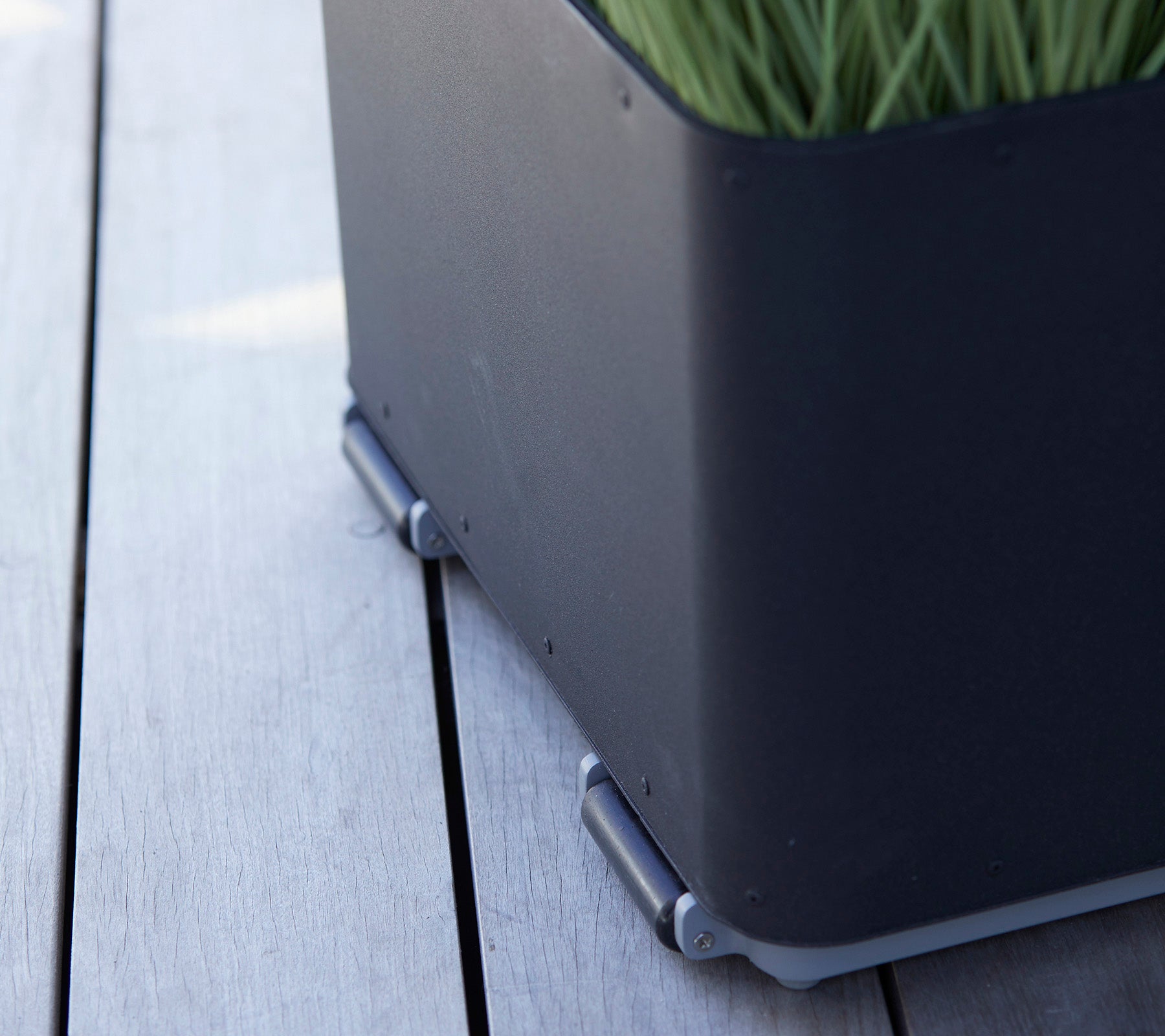 Zwarte plantenbak met een strak ontwerp, met groen gras en zilveren connectoren die op een houten oppervlakte liggen.