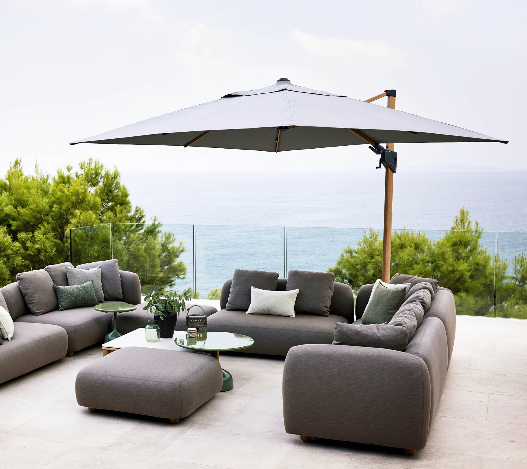 Stijlvolle buitenzitruimte met een grote parasol, grijze sofa's en een glazen tafel met uitzicht op een rustige waterview en weelderig groen.