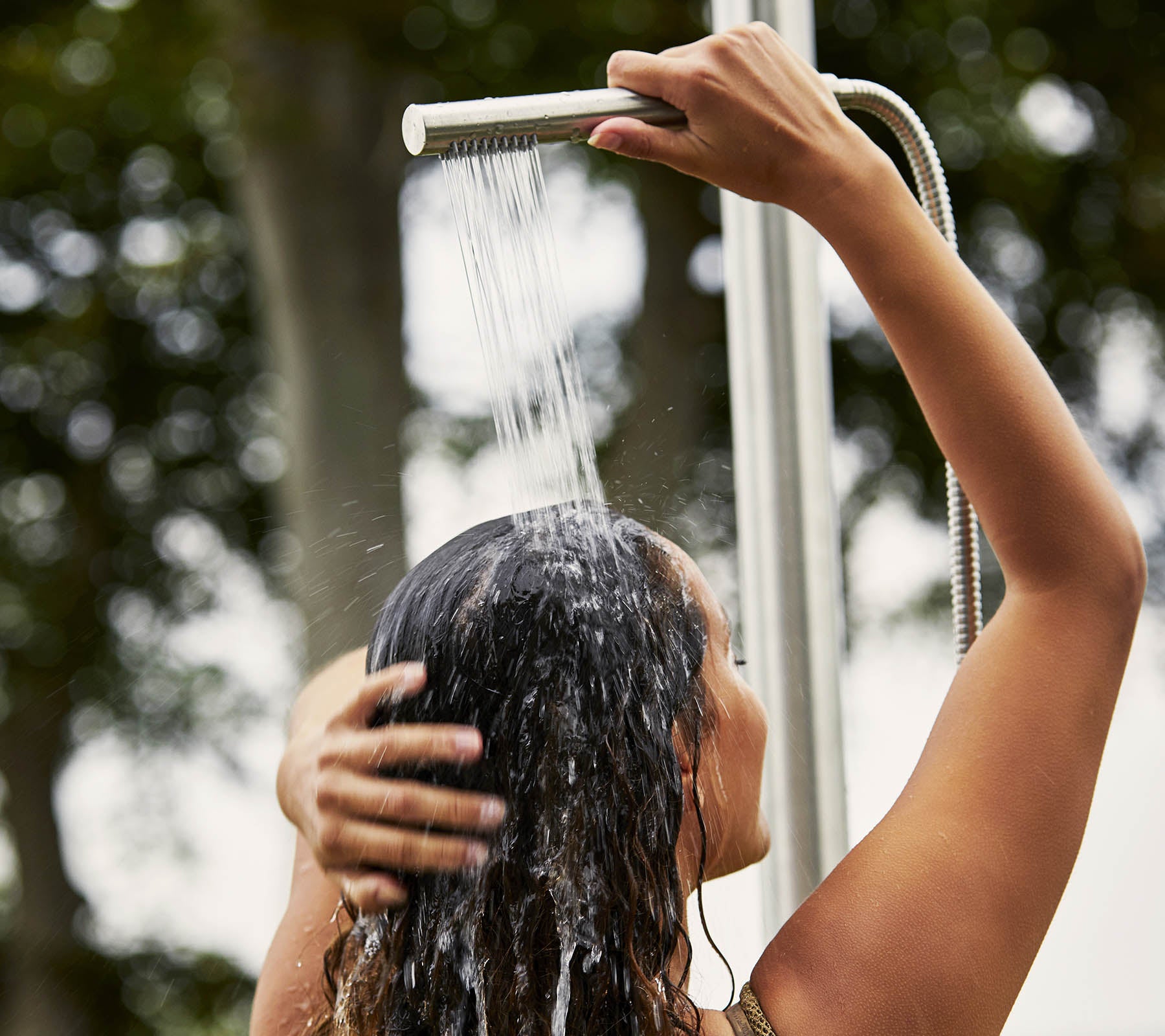 Een persoon die zijn of haar haar wast onder de douche, met water dat naar beneden stroomt en omringd door een natuurlijke omgeving.