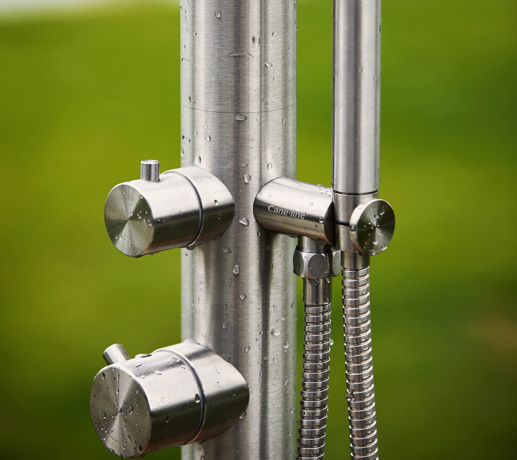 Roestvrijstalen douche eenheid met twee knoppen voor temperatuurregeling en een handdouche, tegen een groene achtergrond.