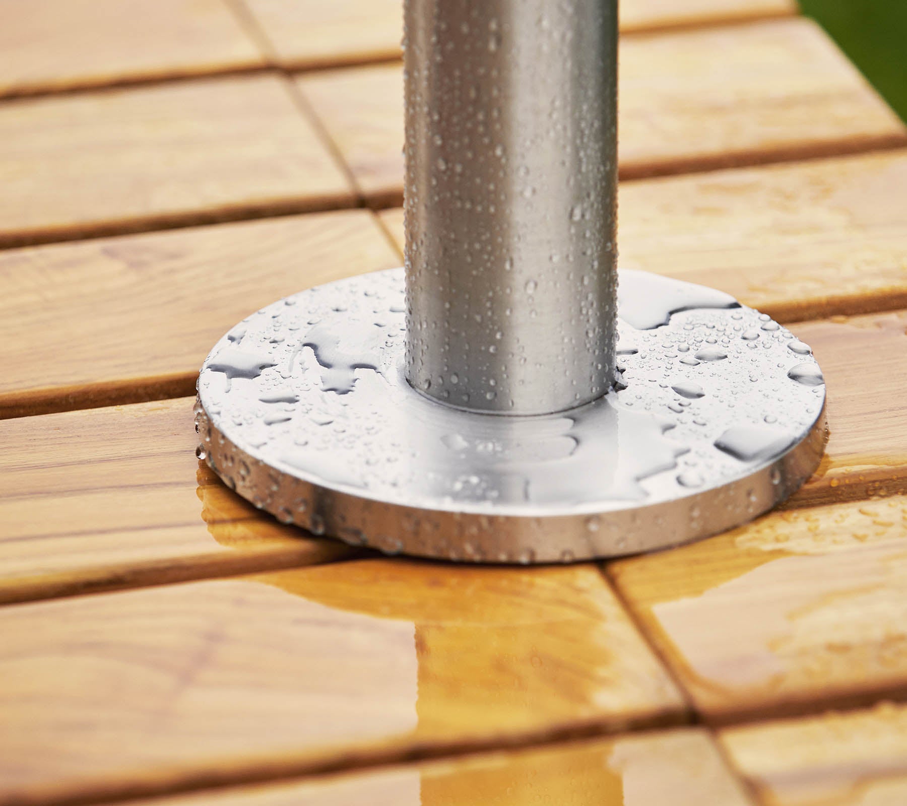 Metalen basis met een paal die op een houten oppervlak rust, met waterdruppels op zowel de basis als het hout.