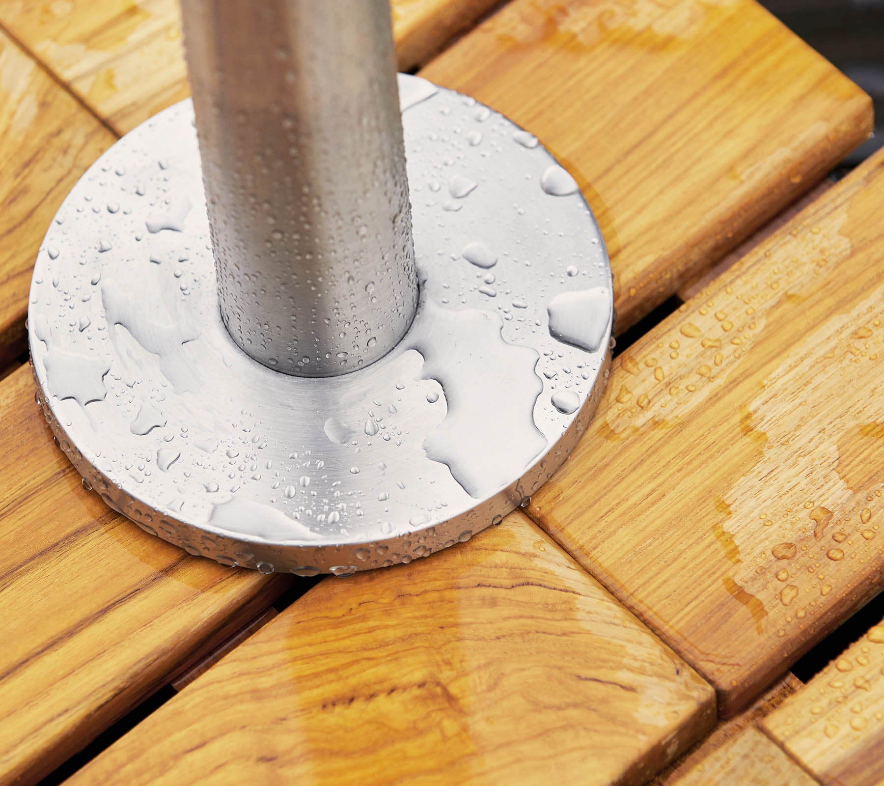Metalen basis met waterdruppels die op een houten oppervlak rusten, met gladde, gebaande planken en een cilindrische paal in het midden.