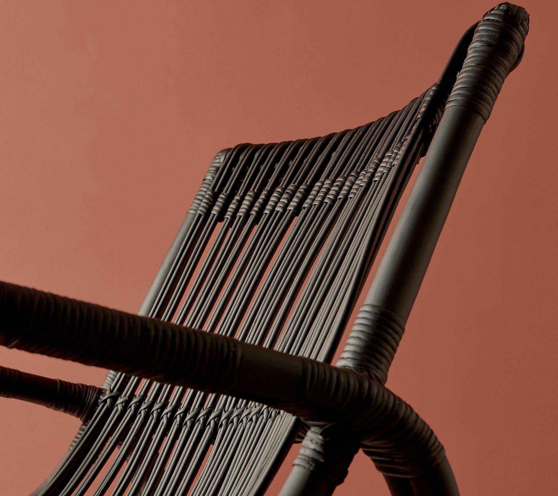 Een close-up van een gevlochten stoelrugleuning tegen een warmgekleurde achtergrond, die het ingewikkelde ontwerp en de textuur benadrukt.