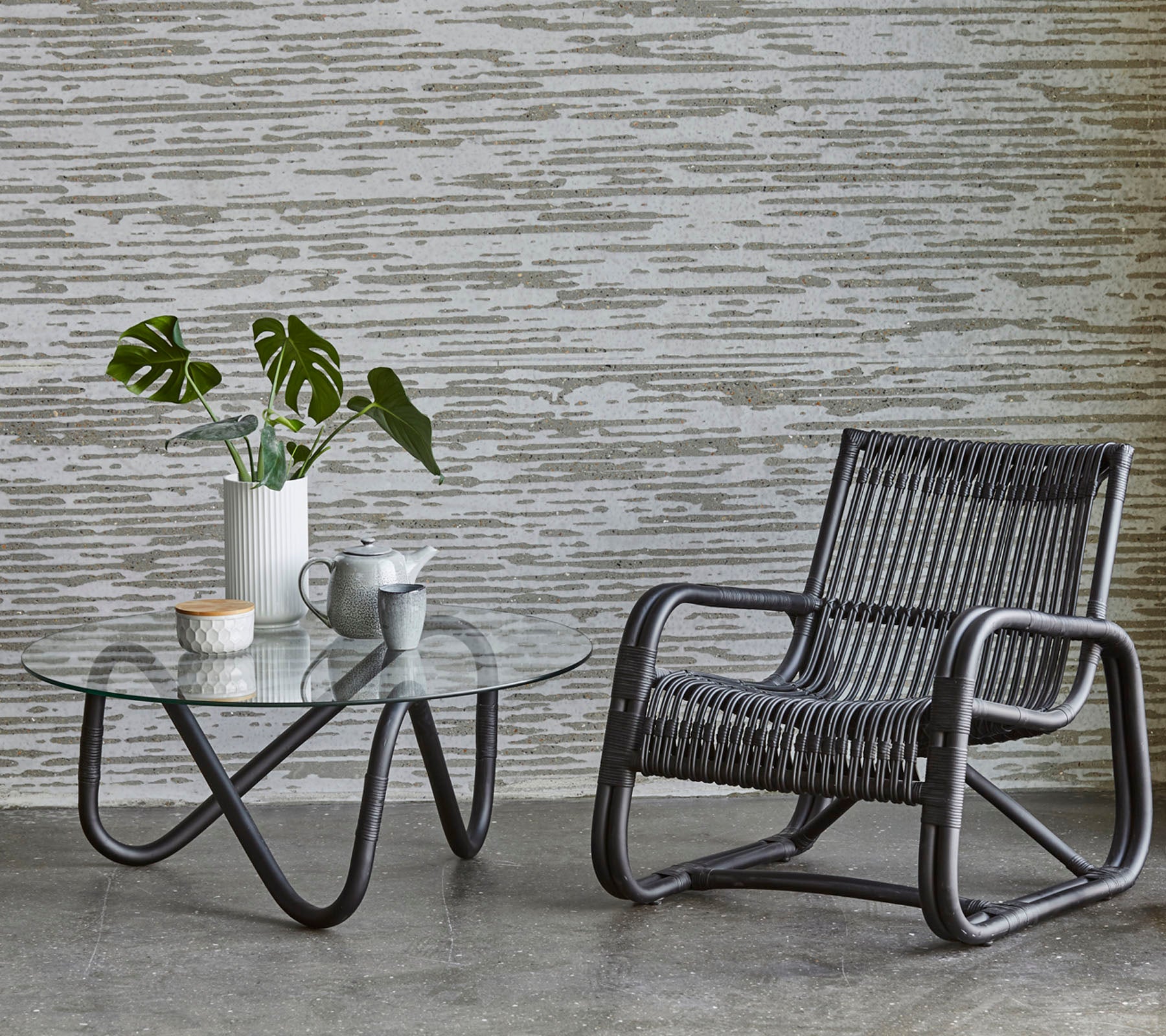 Een stijlvolle stoel en een tafel met een glazen blad met een plant en koffie, aangevuld met een gestructureerde muur in de achtergrond.