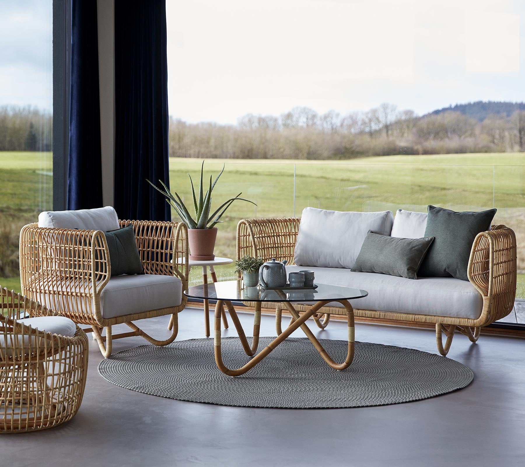 Een stijlvolle zithoek met geweven meubels, een rond tapijt en een glazen salontafel, aangevuld met minimalistische decoratieve elementen.