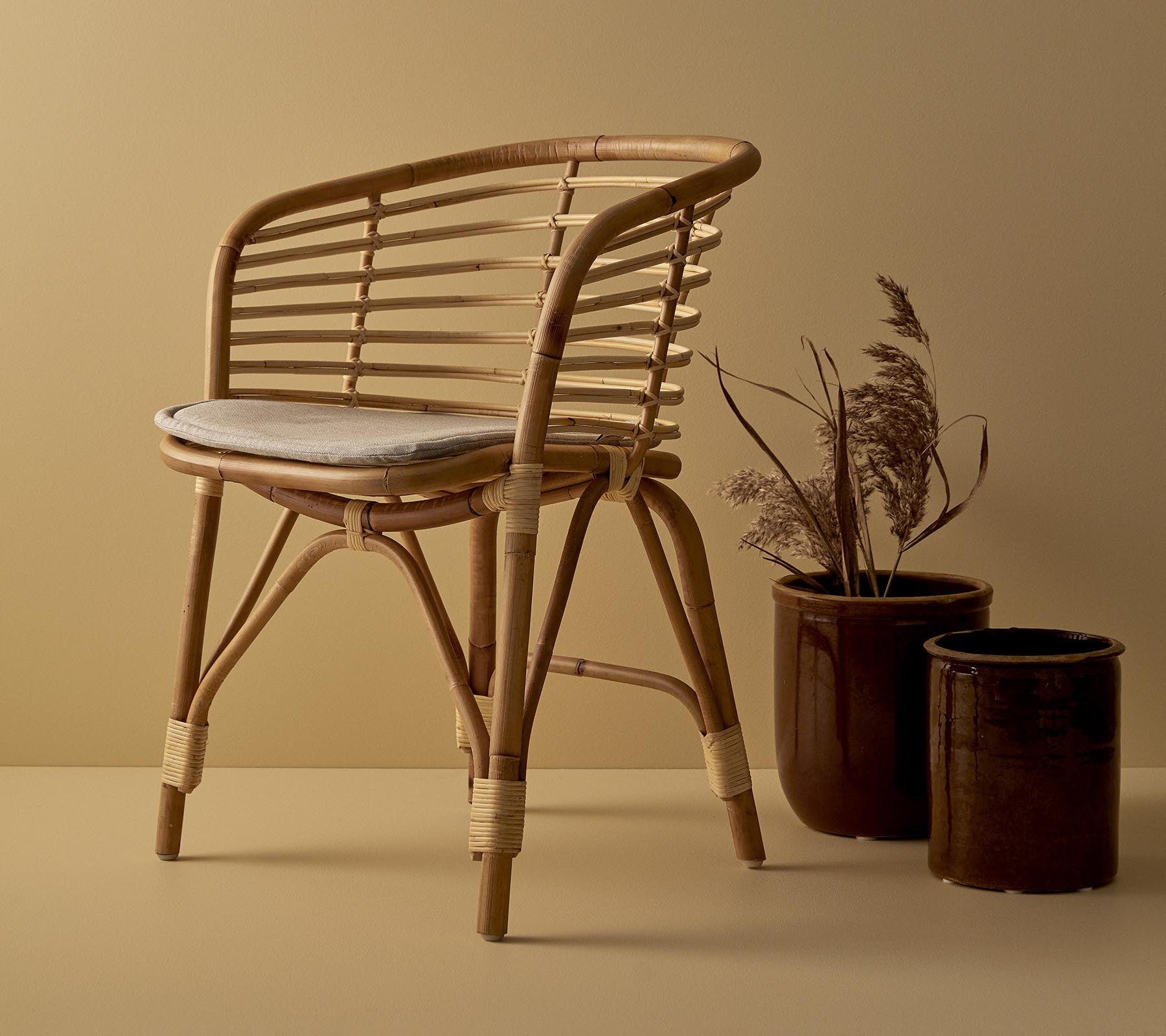 Een stijlvolle rieten stoel met een gewatteerde zitting, vergezeld van twee decoratieve plantenpotten met gedroogde planten.
