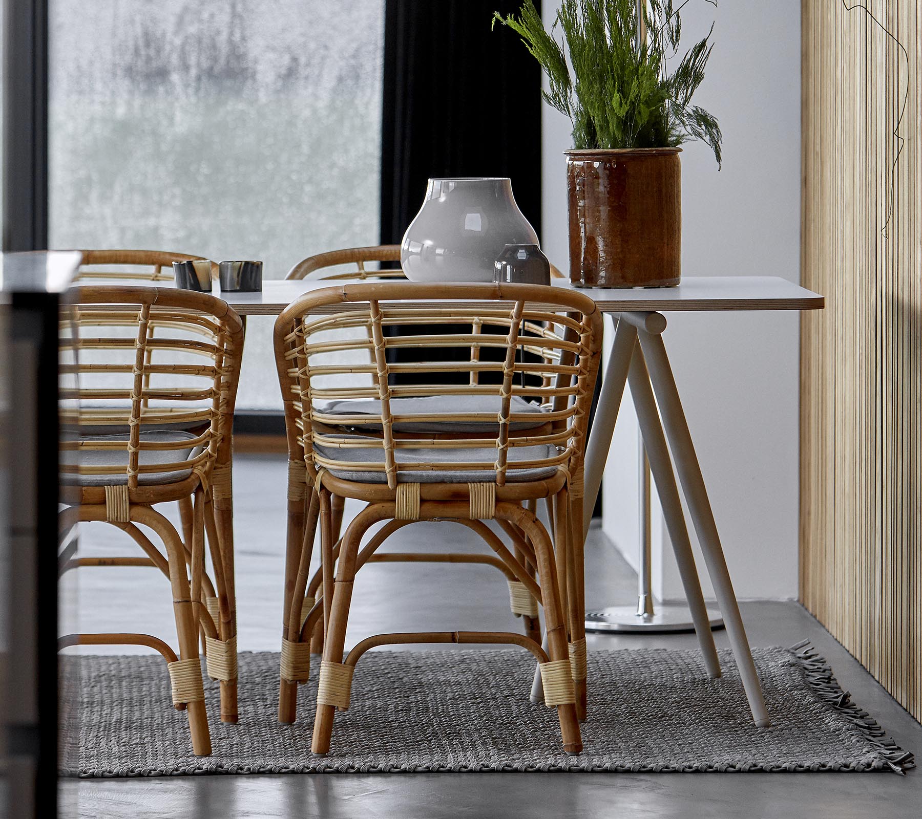 Een moderne eethoek met rotan stoelen, een strak tafel en decoratieve groen in een stijlvol interieur.