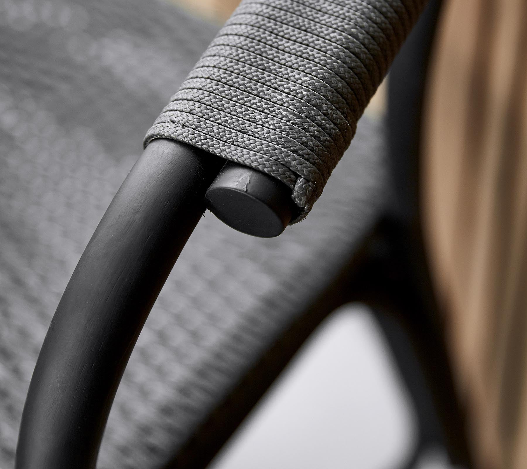Close-up van de armleuning van een stijlvolle stoel met een slank zwart frame en een gestructureerde grijze omhulsel voor een comfortabele grip.