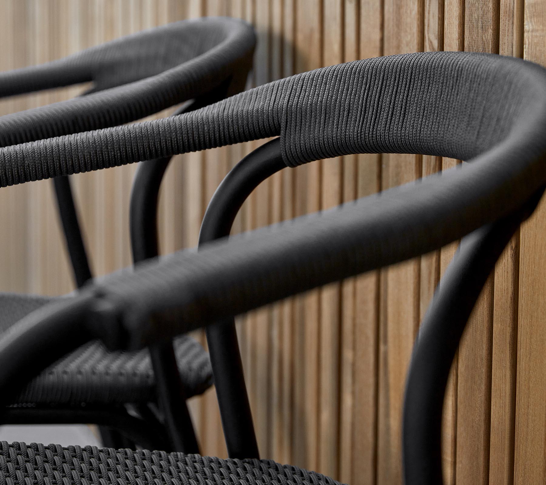 Drie stijlvolle zwarte stoelen met gebogen armen, ontworpen met een gestructureerde afwerking, tegen een warme houten achtergrond.