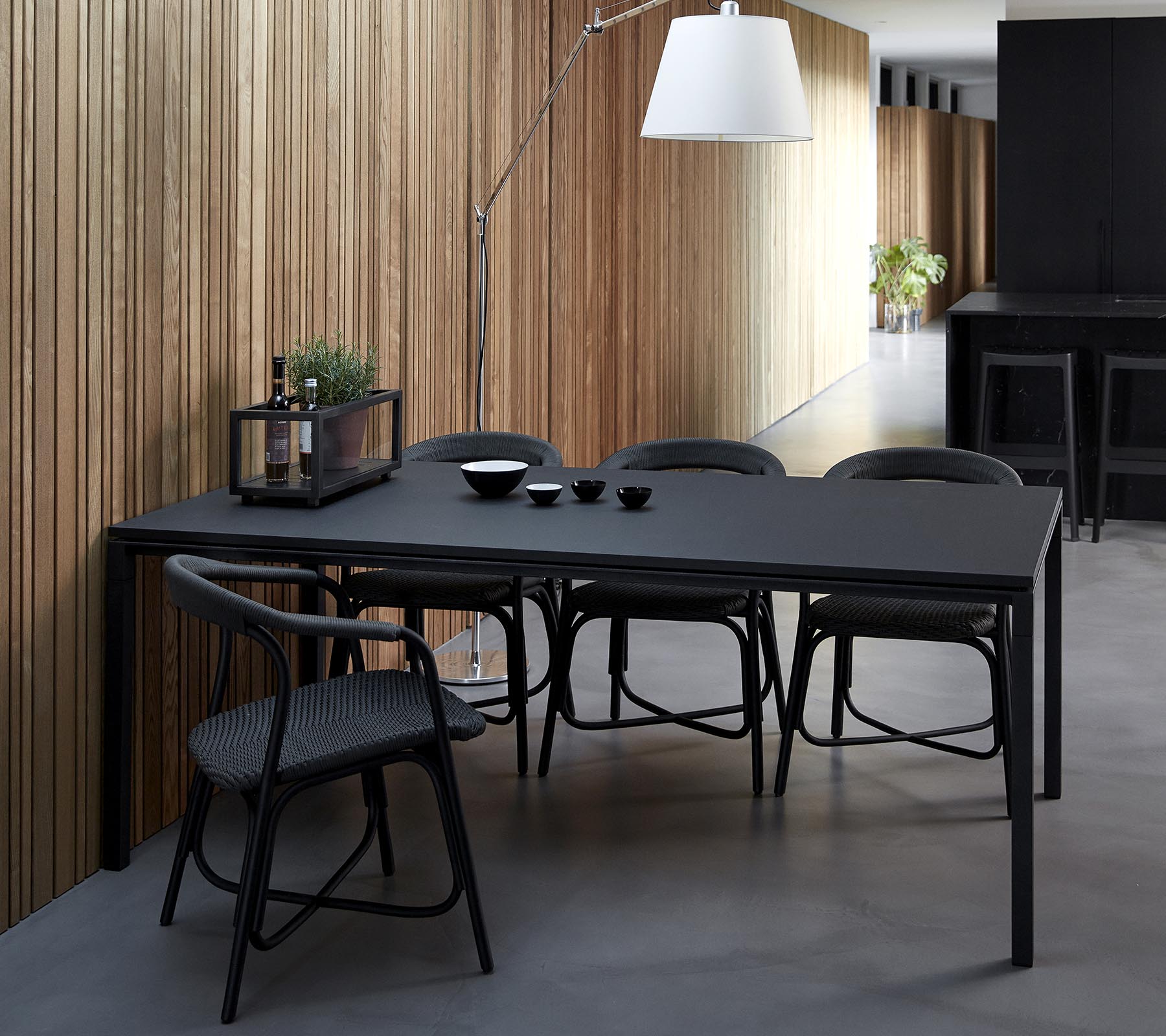 Een slank zwart eettafel vergezeld van stoelen, gedekt met kommen en decoratieve artikelen, tegen een achtergrond van houten panelen.