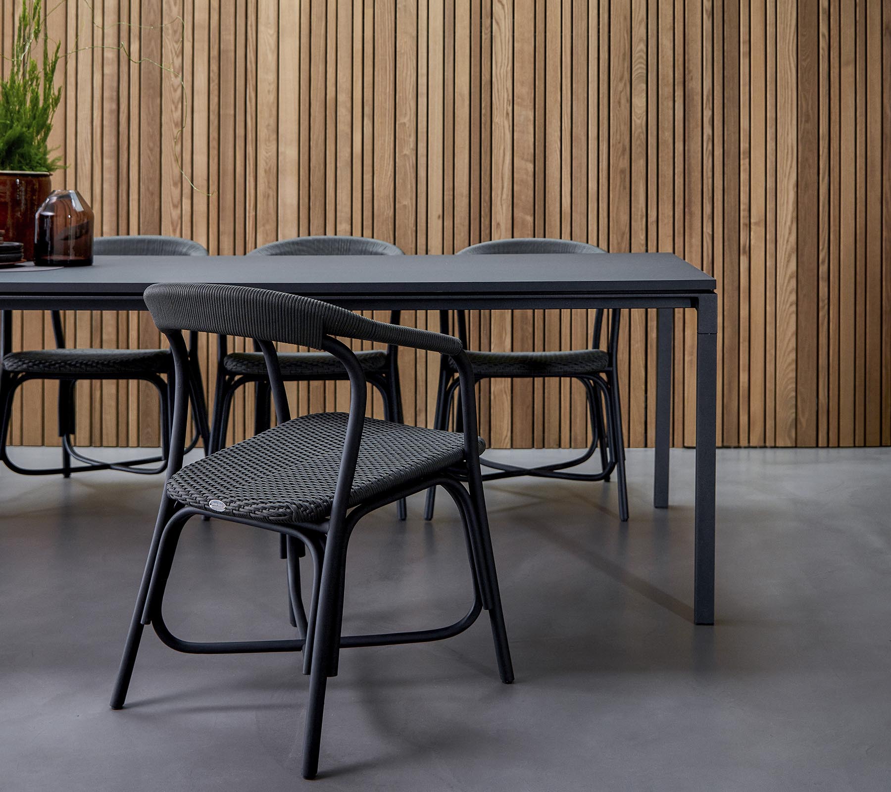 Een moderne eetruimte met een strak tafel omringd door stijlvolle stoelen, tegen een gestructureerde houten achtergrond.