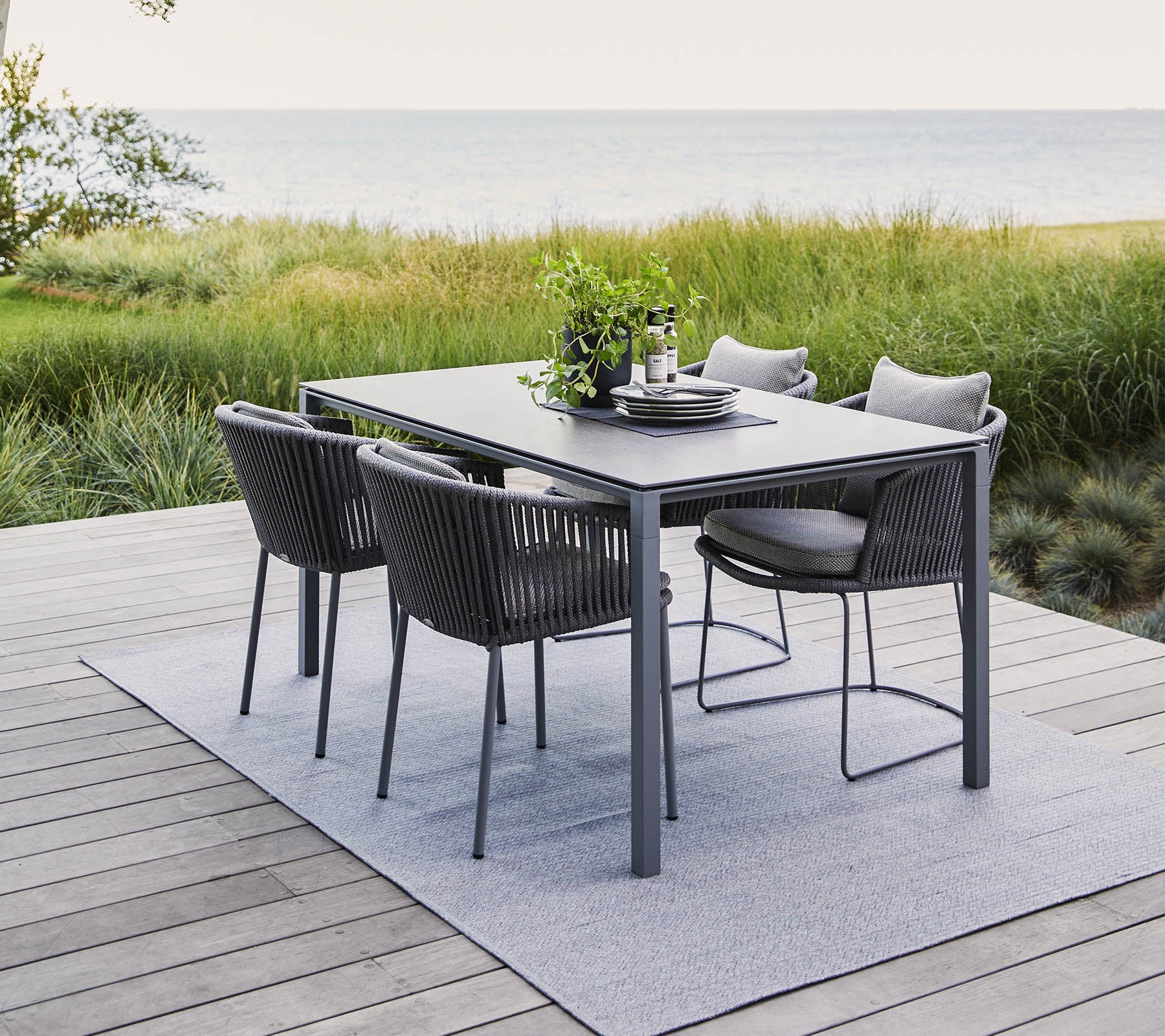 Een modern buitentafelsset met een rechthoekige tafel en vier stijlvolle stoelen, omringd door groen en een sereen uitzicht op water.