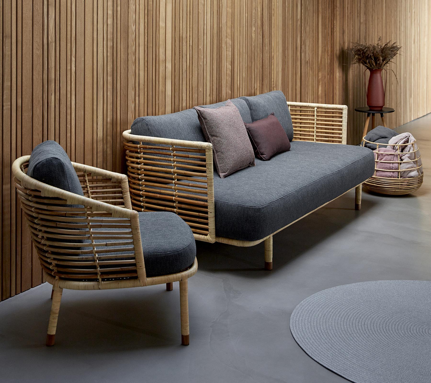 Stijlvolle zithoek met een grijze gestoffeerde bank met houten accenten en een bijpassende stoel, aangevuld met decoratieve kussens.