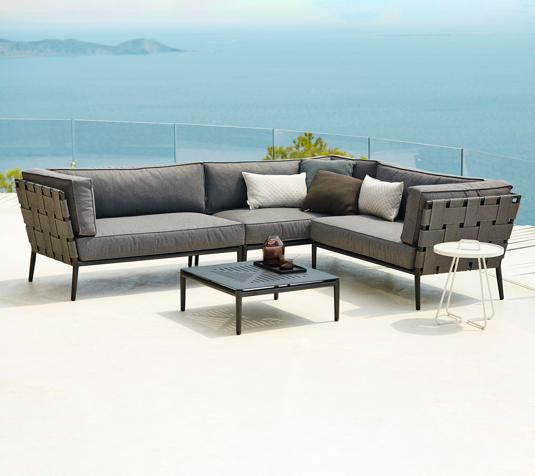 Moderne buitenzitarrangement met een sectie sofa met kussens en een salontafel, met een schilderachtige achtergrond van water.