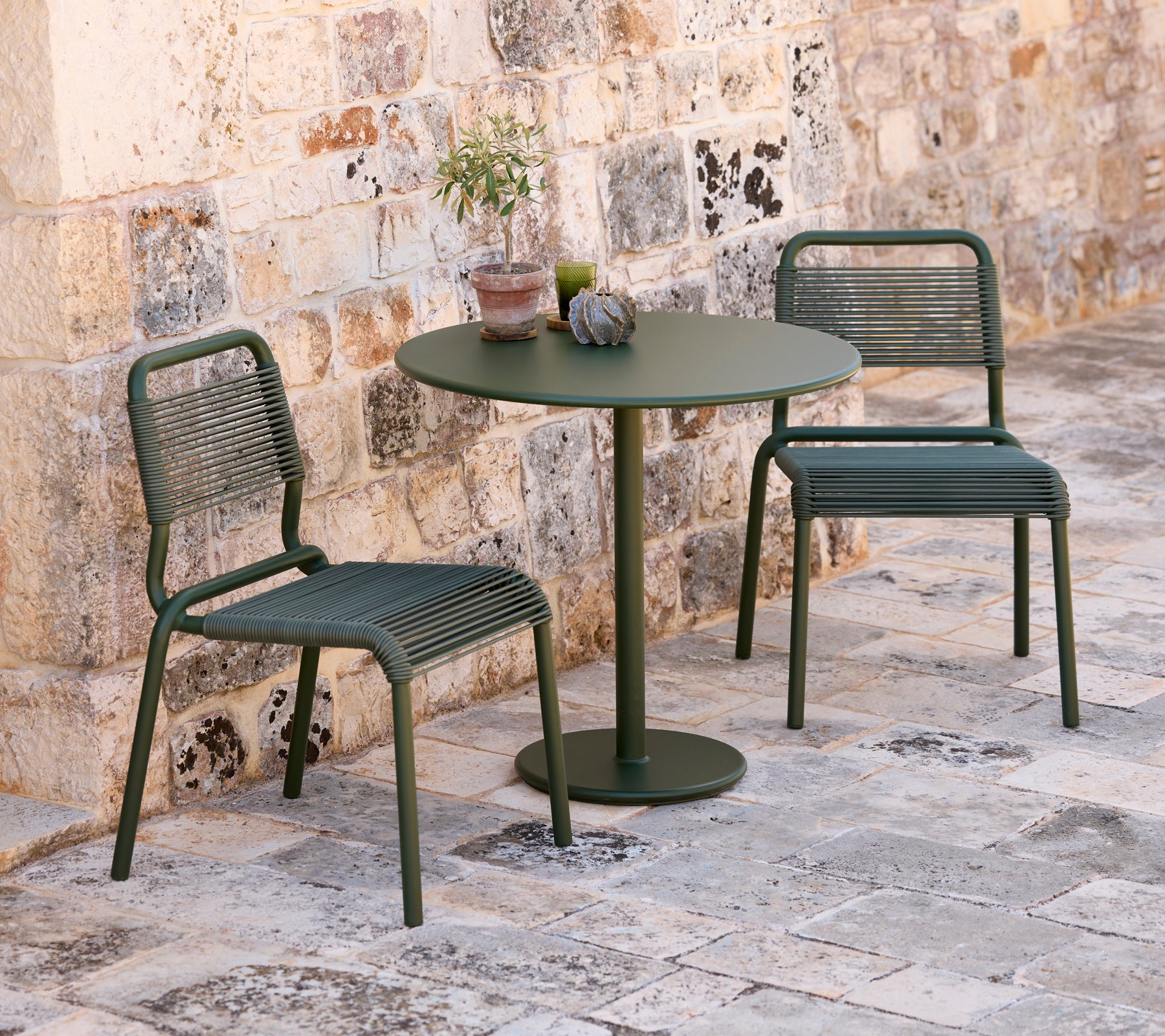 Twee groene stoelen en een ronde groene tafel in een buitenomgeving.