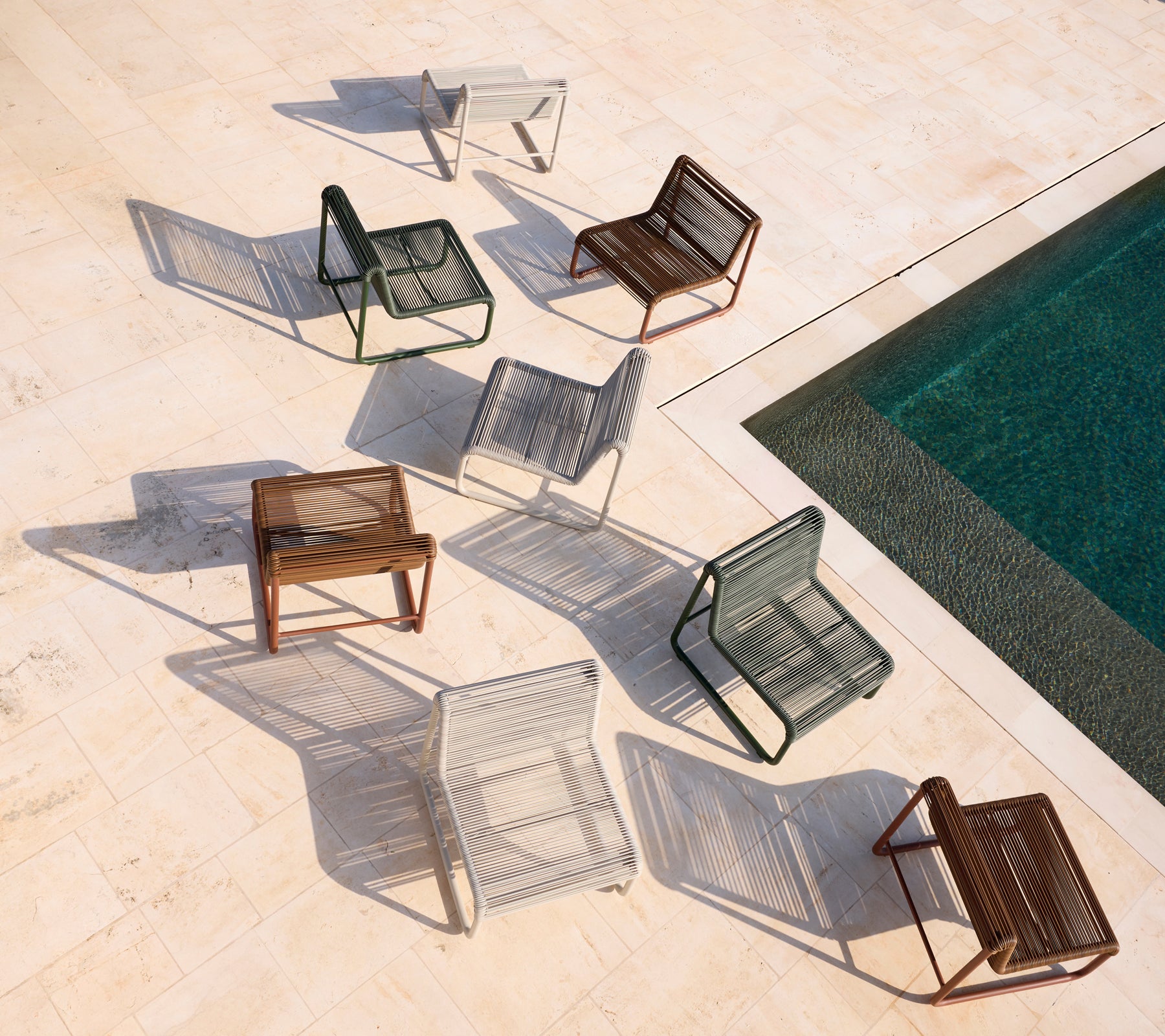 Diverse moderne stoelen in bruin, grijs, wit en zwart rond een zwembad gerangschikt.