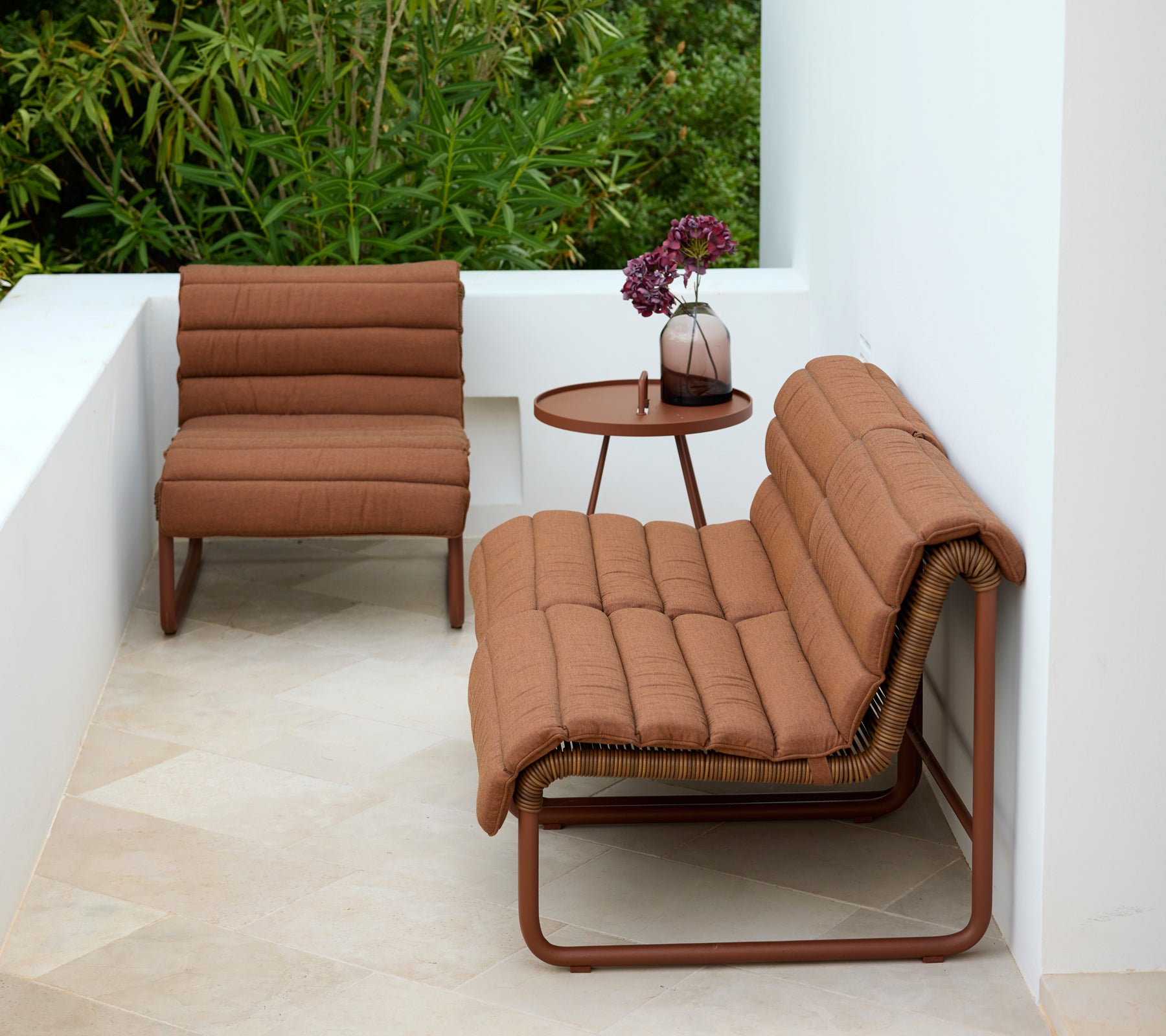 Bruine lounge fauteuil en loveseat met een ronde bijzettafel in een moderne buitensetting.