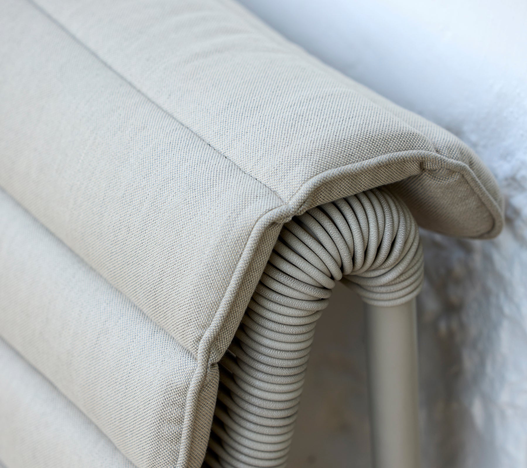 Beige kussen met een ribbeltextuur dat tegen een lichte muur leunt.