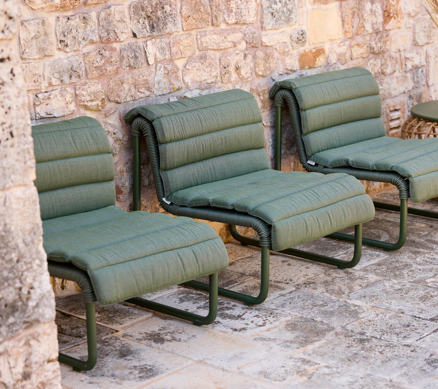 Groene loungestoelen staan tegen een stenen muur.