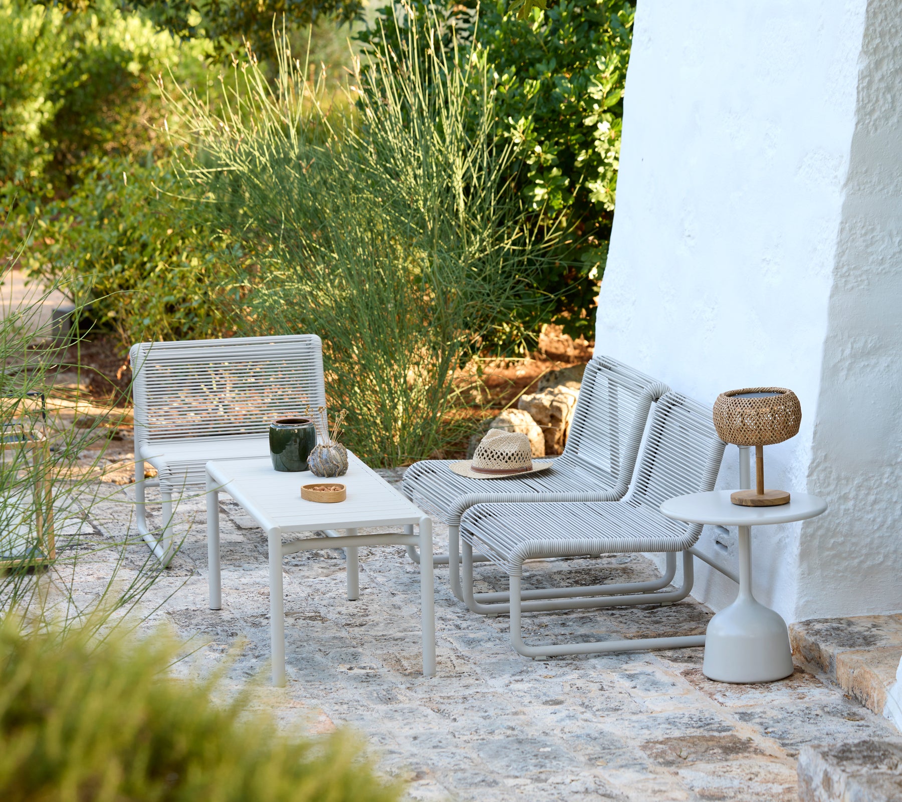 Moderne grijze lounge stoelen en witte tafels in een minimalistische buitenomgeving.