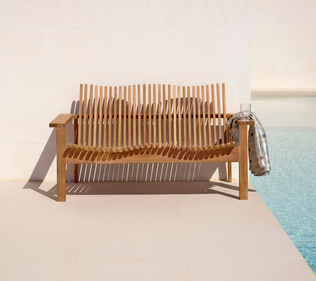 Stijlvolle houten 2-zitsbank met lattenontwerp, aangevuld met een gezellig deken, naast een rustige pool. Perfect voor ontspanning.